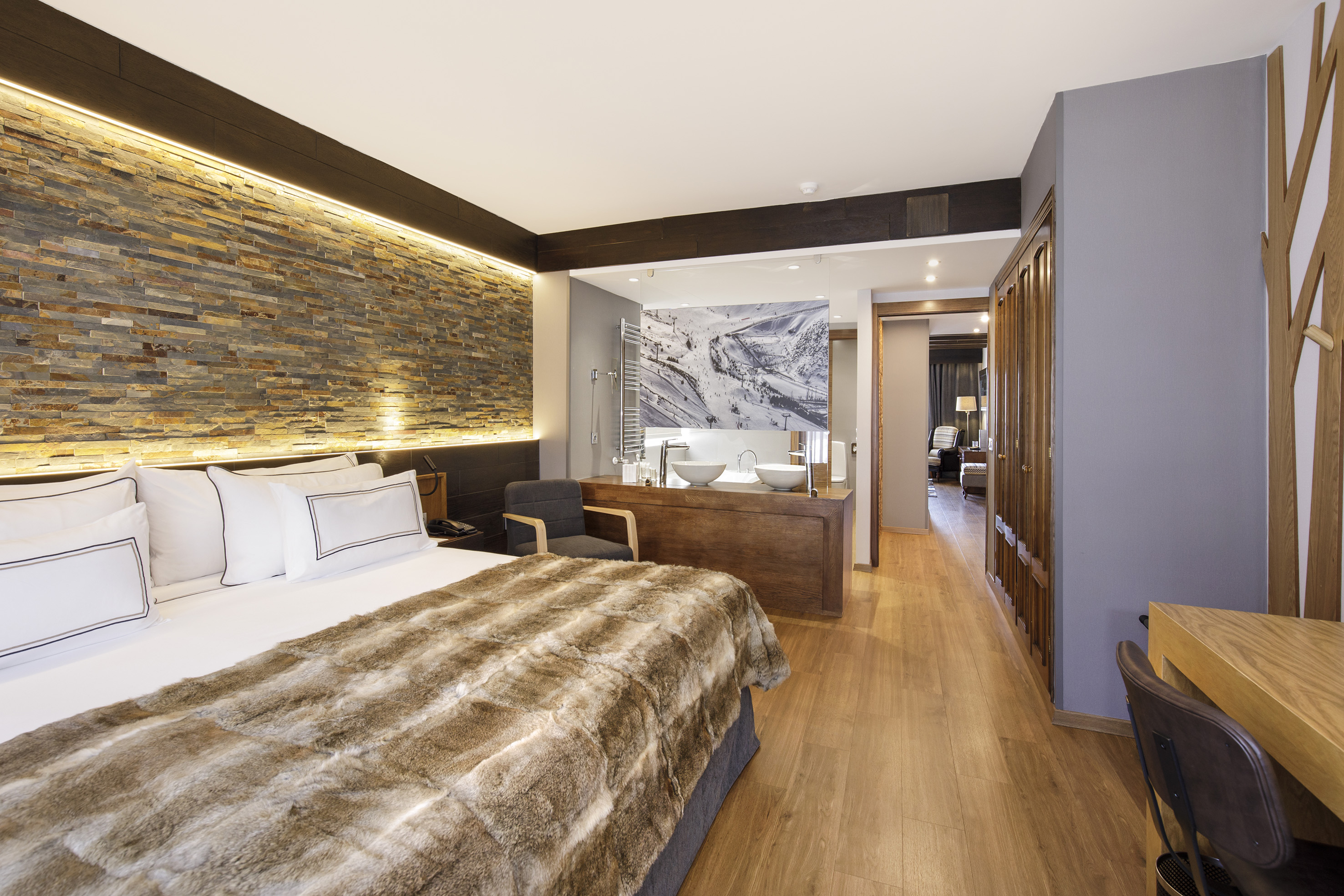 Modern hotel bedroom with stone wall, furry bedspread, wood floor, ski mural.