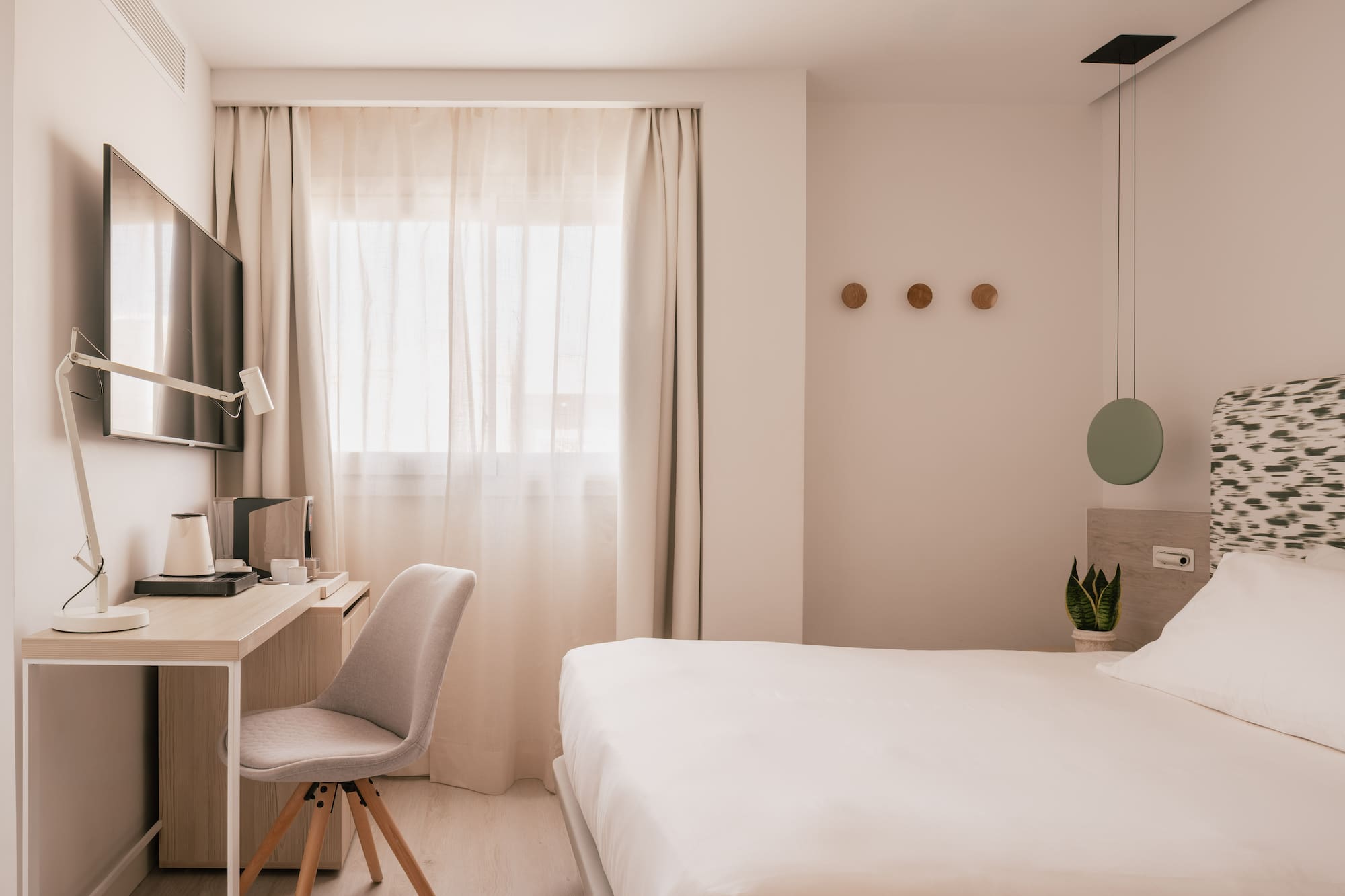 Habitación de hotel moderna con cama, escritorio, TV y decoración minimalista.