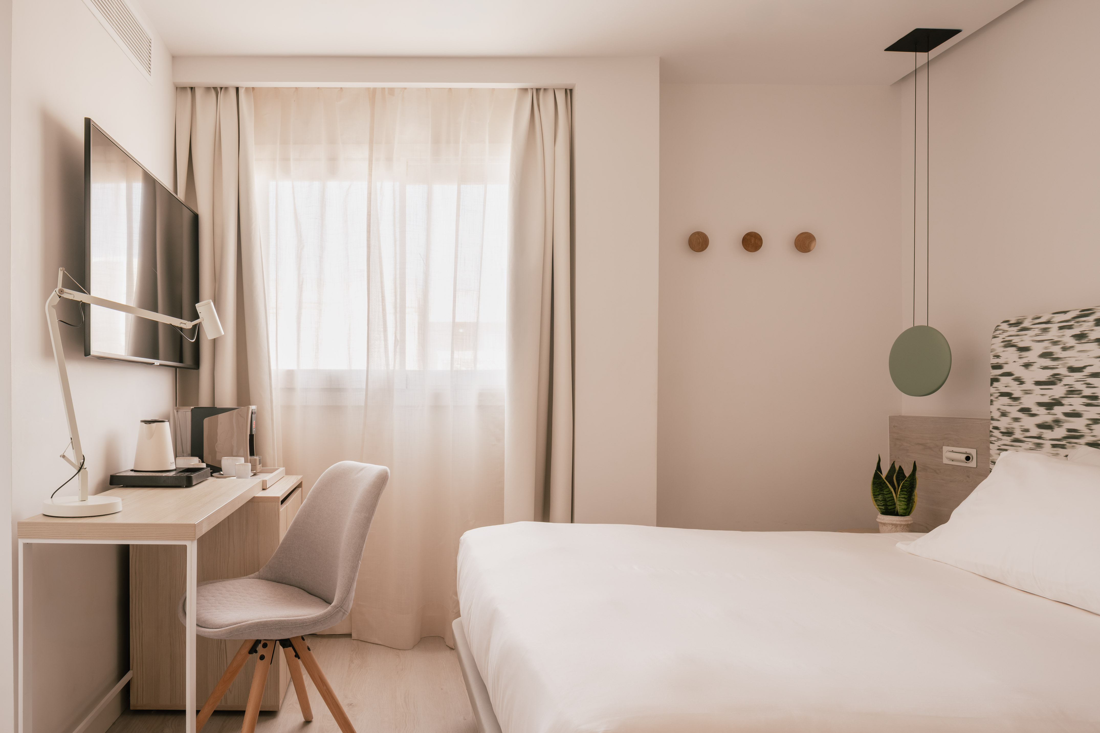 Habitación de hotel moderna con cama, escritorio, TV y decoración minimalista.