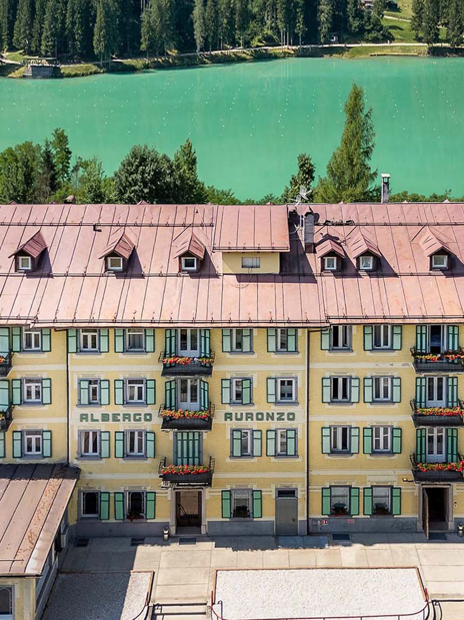 Albergo Auronzo hotel overlooking turquoise lake and green forest.