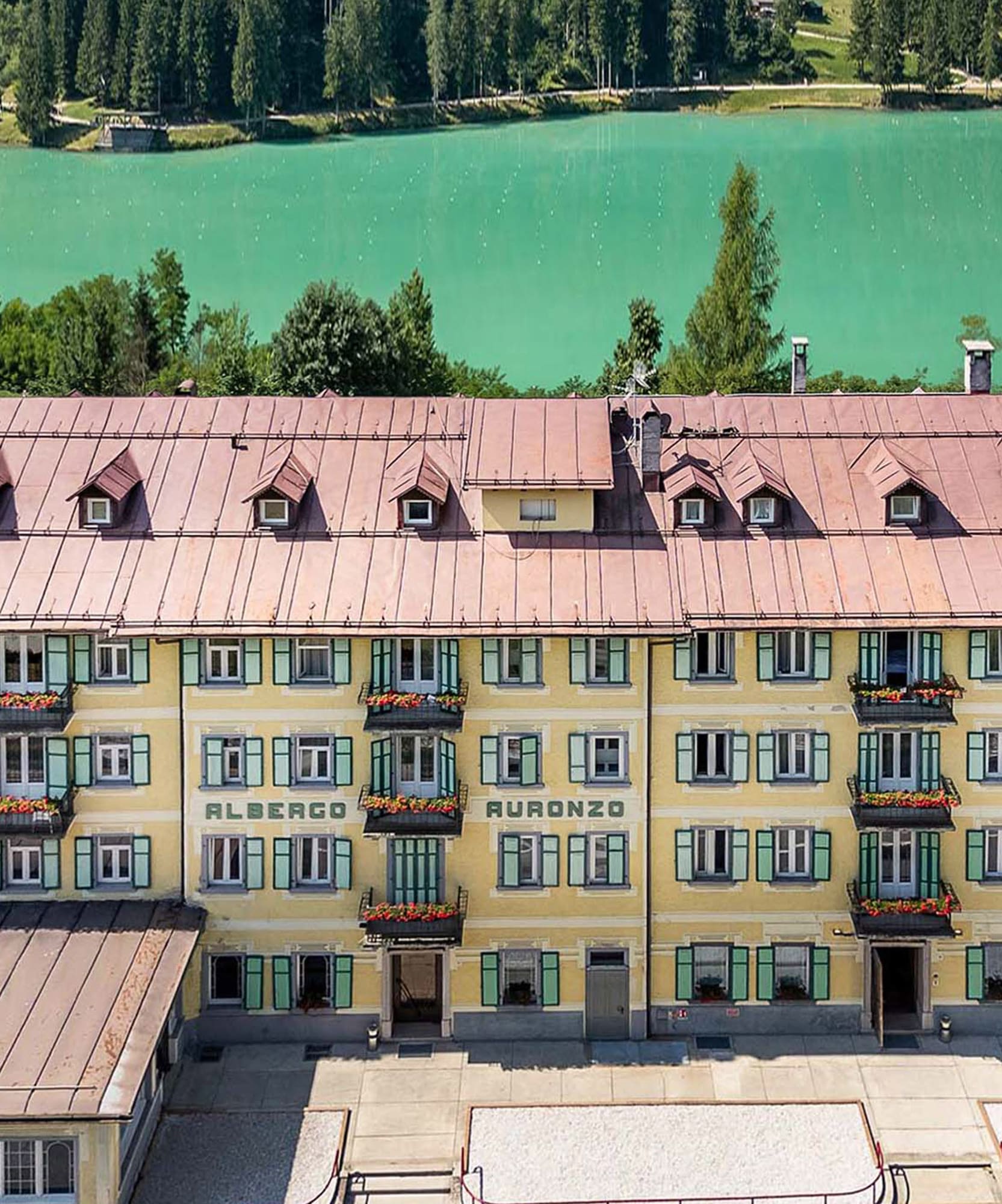 Albergo Auronzo hotel overlooking turquoise lake and green forest.