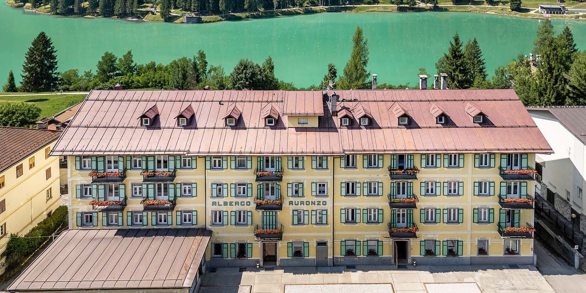 Albergo Auronzo hotel overlooking turquoise lake and pine forest.