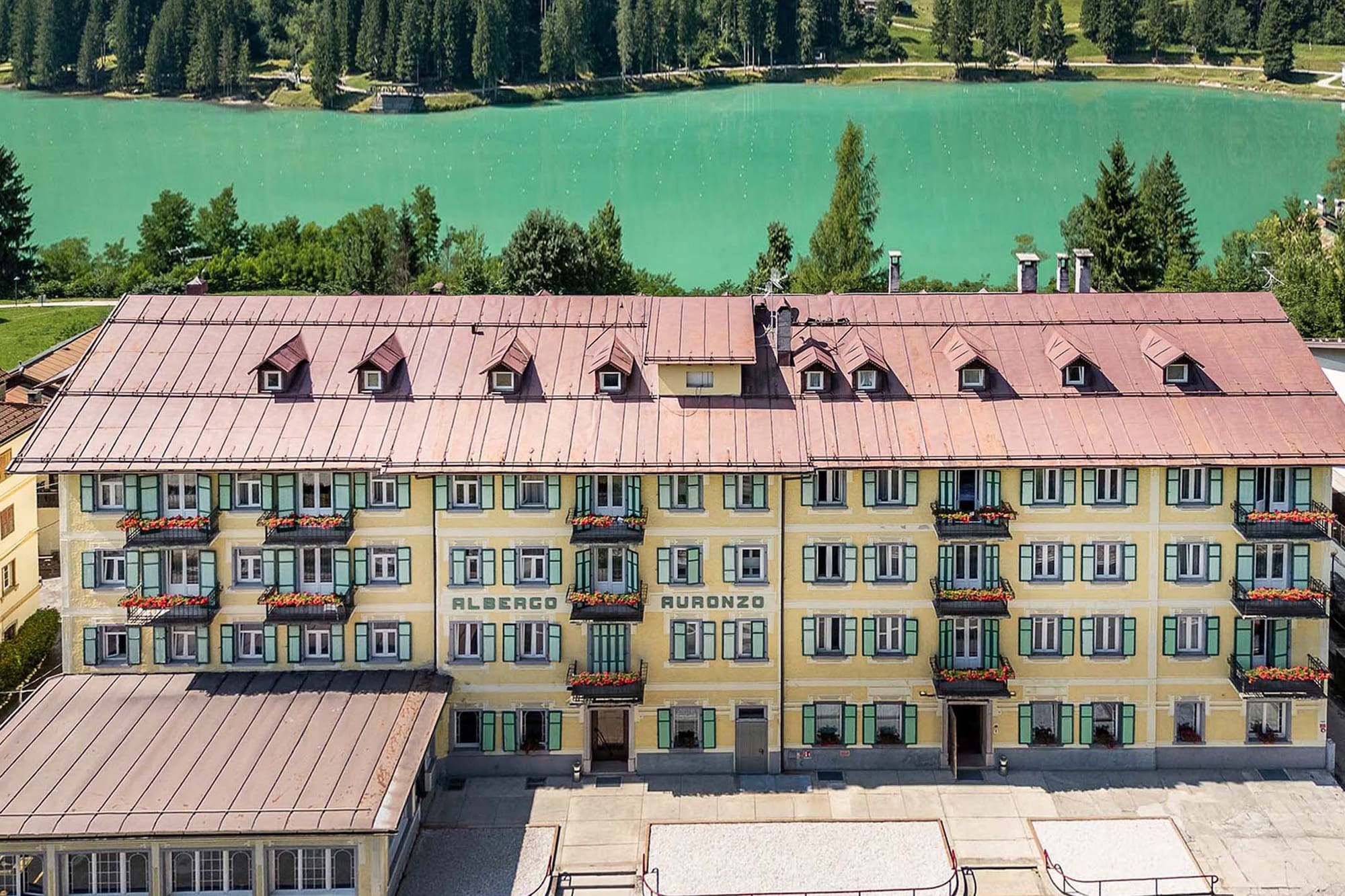 Albergo Auronzo hotel, yellow facade, red roof, turquoise lake, Dolomites.