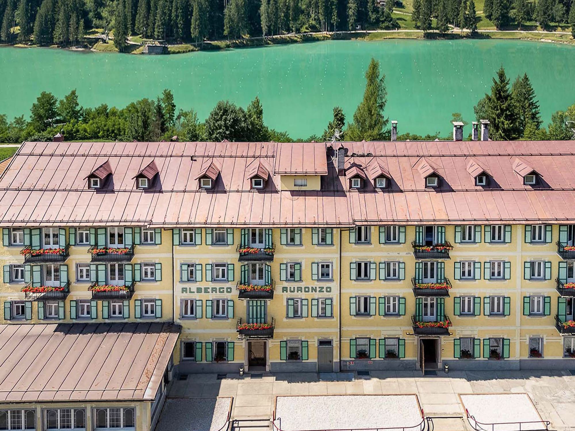 Albergo Auronzo hotel overlooking turquoise lake and pine forest.