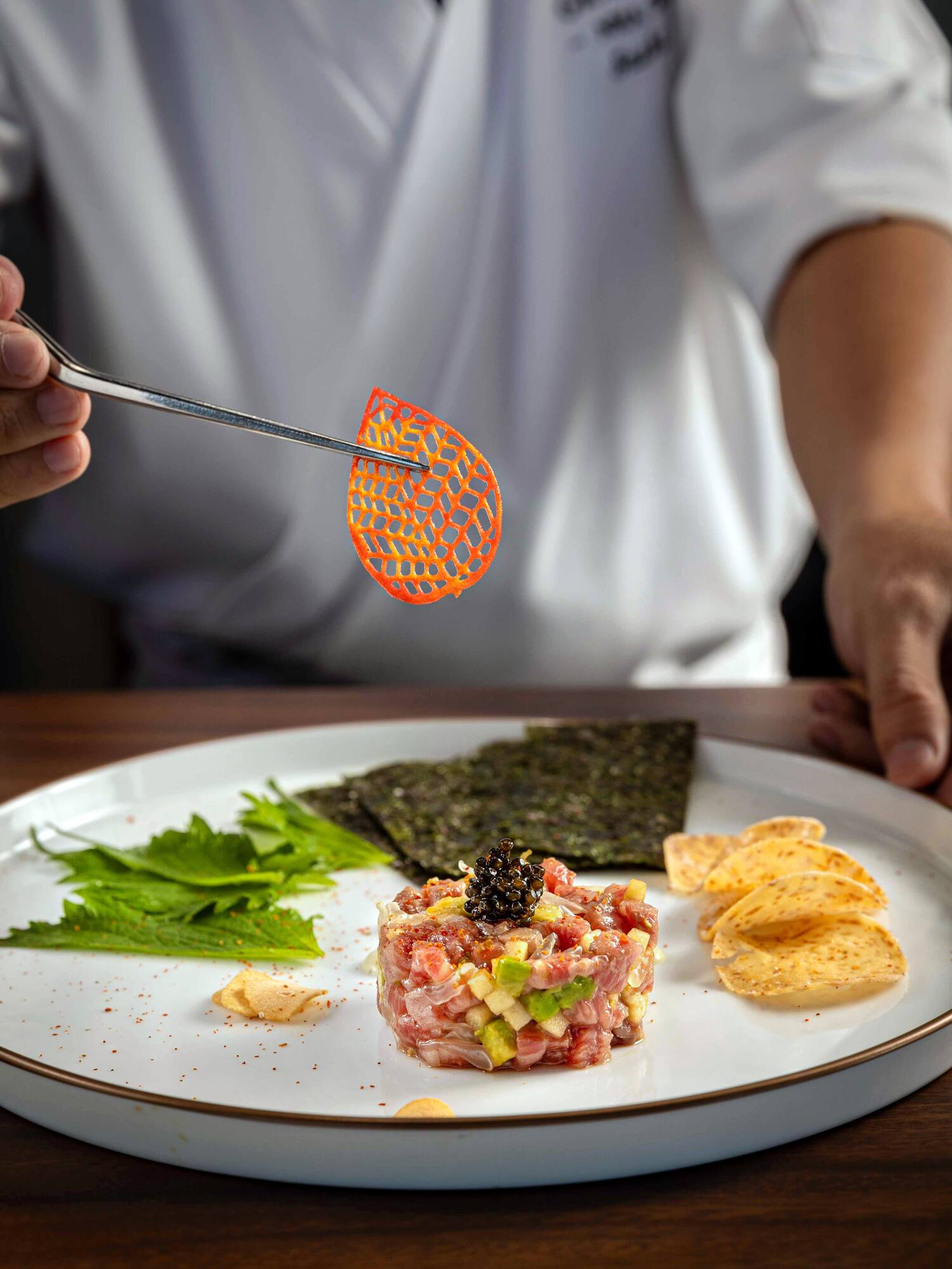 Chef garnishing gourmet tuna tartare with caviar, avocado, and orange chip.