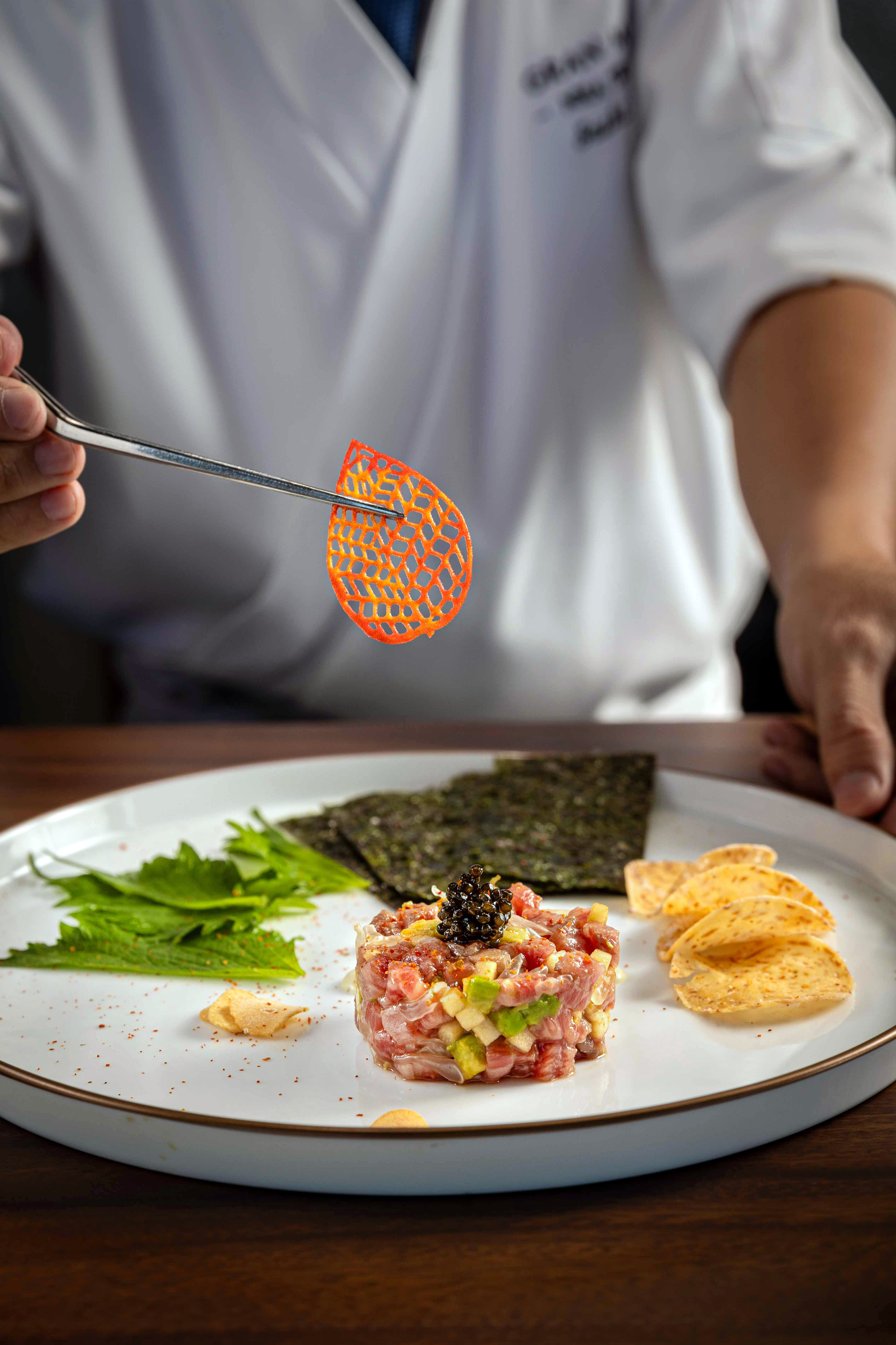 Chef garnishing gourmet tuna tartare with caviar, avocado, and orange chip.