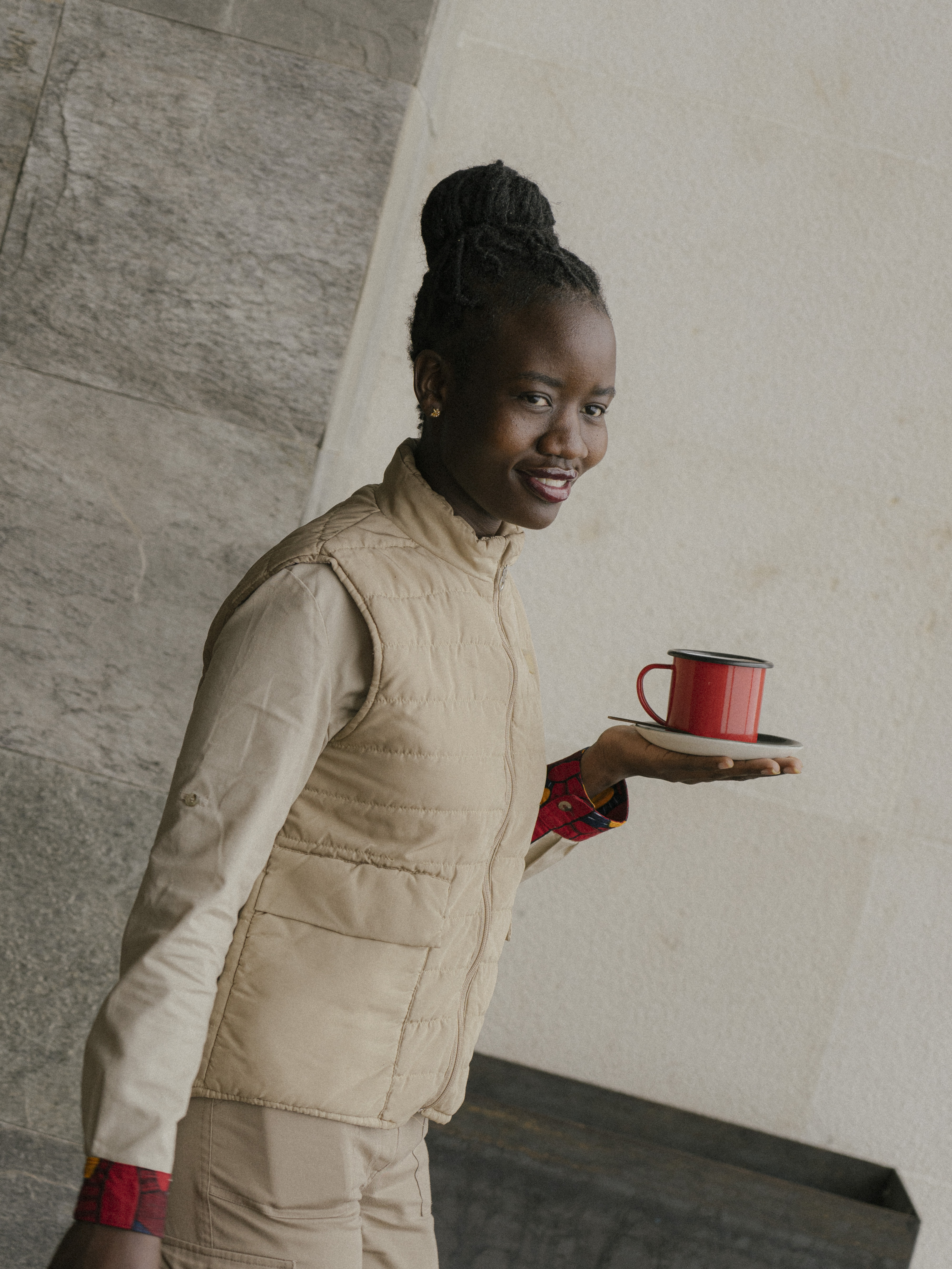 Smiling woman holding red coffee mug, wearing a beige puffer vest.