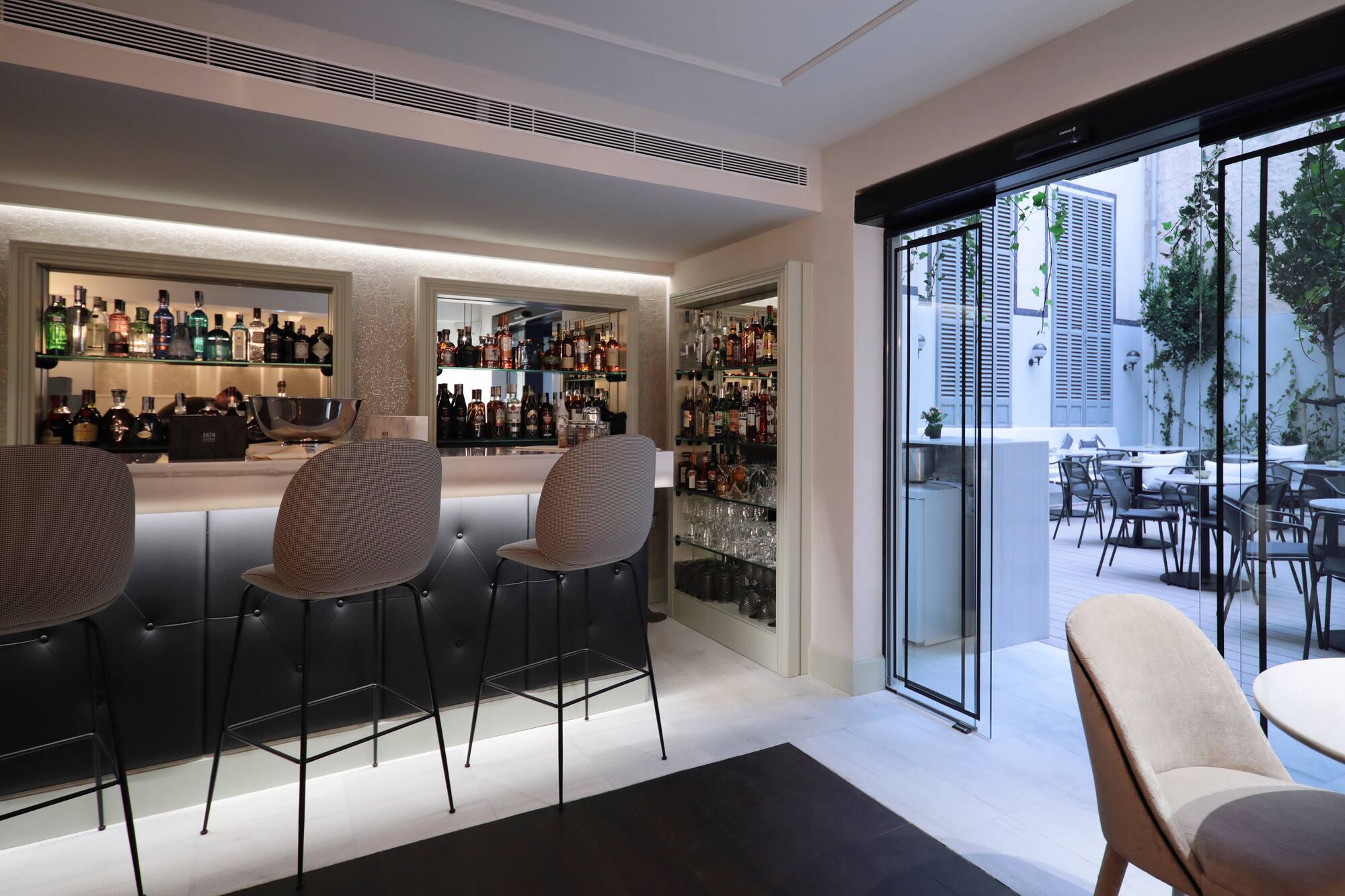 Contemporary bar with bottles and stools, connecting to an outdoor patio.