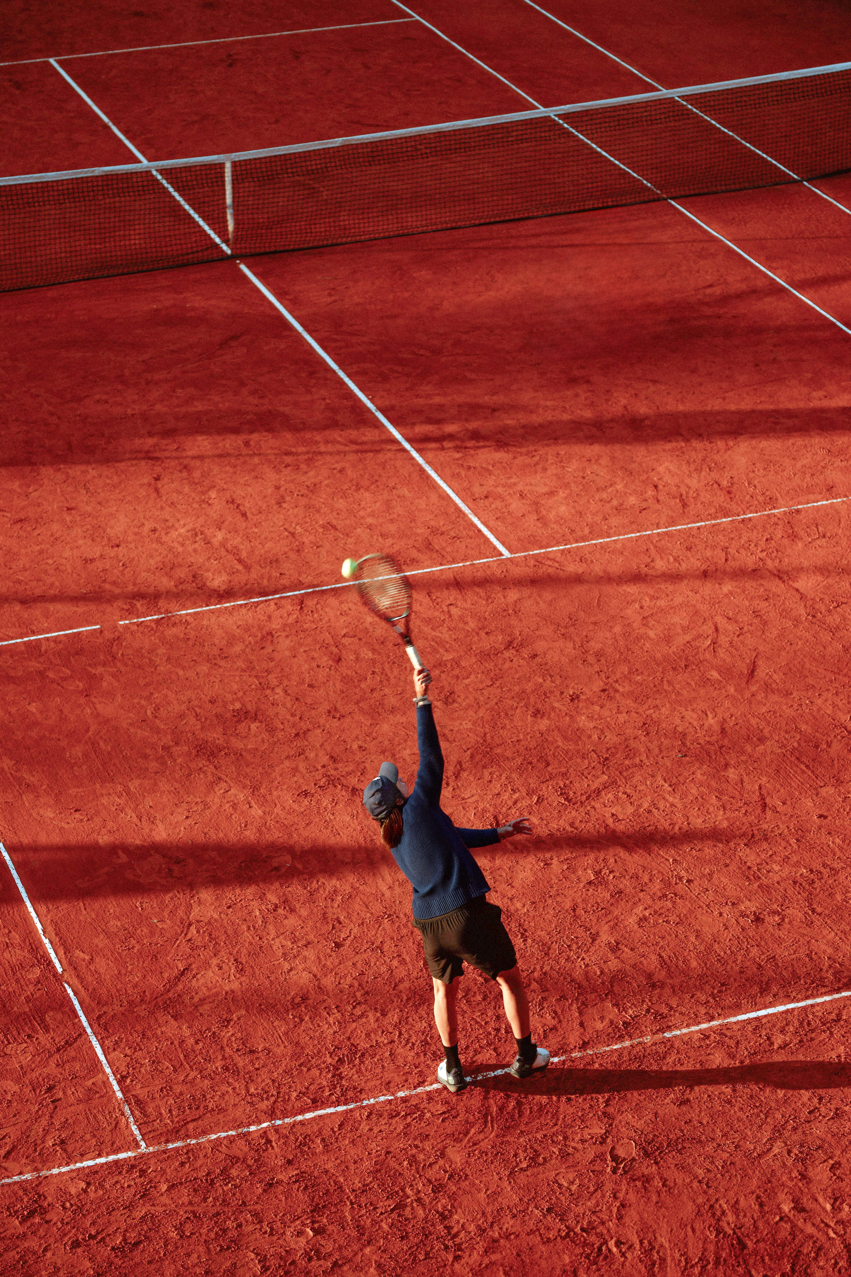 Overhead view of a tennis player serving on a red clay court.