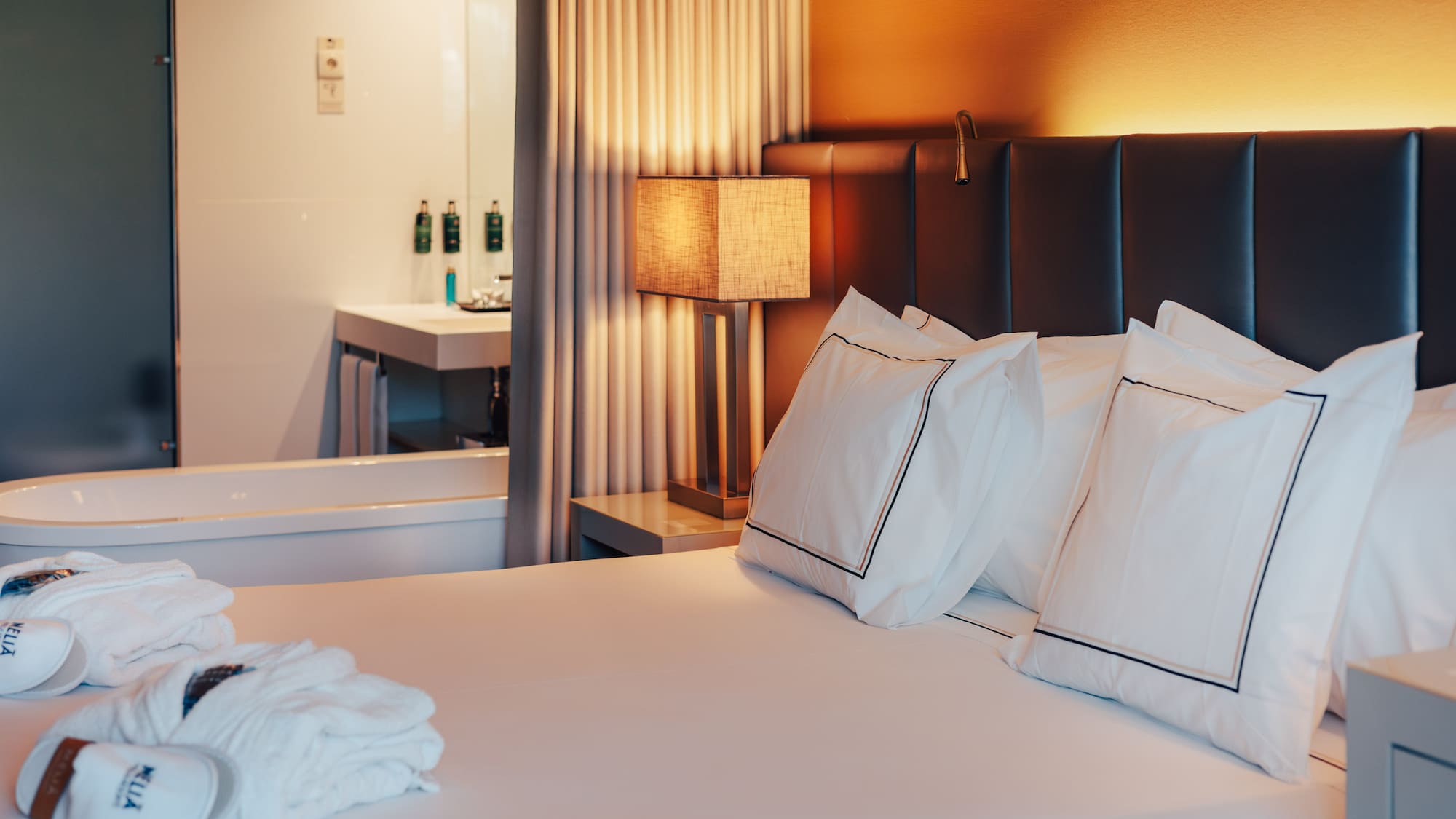 Elegant Meliá hotel room with bed, warm lamp, robes, and visible bathtub.