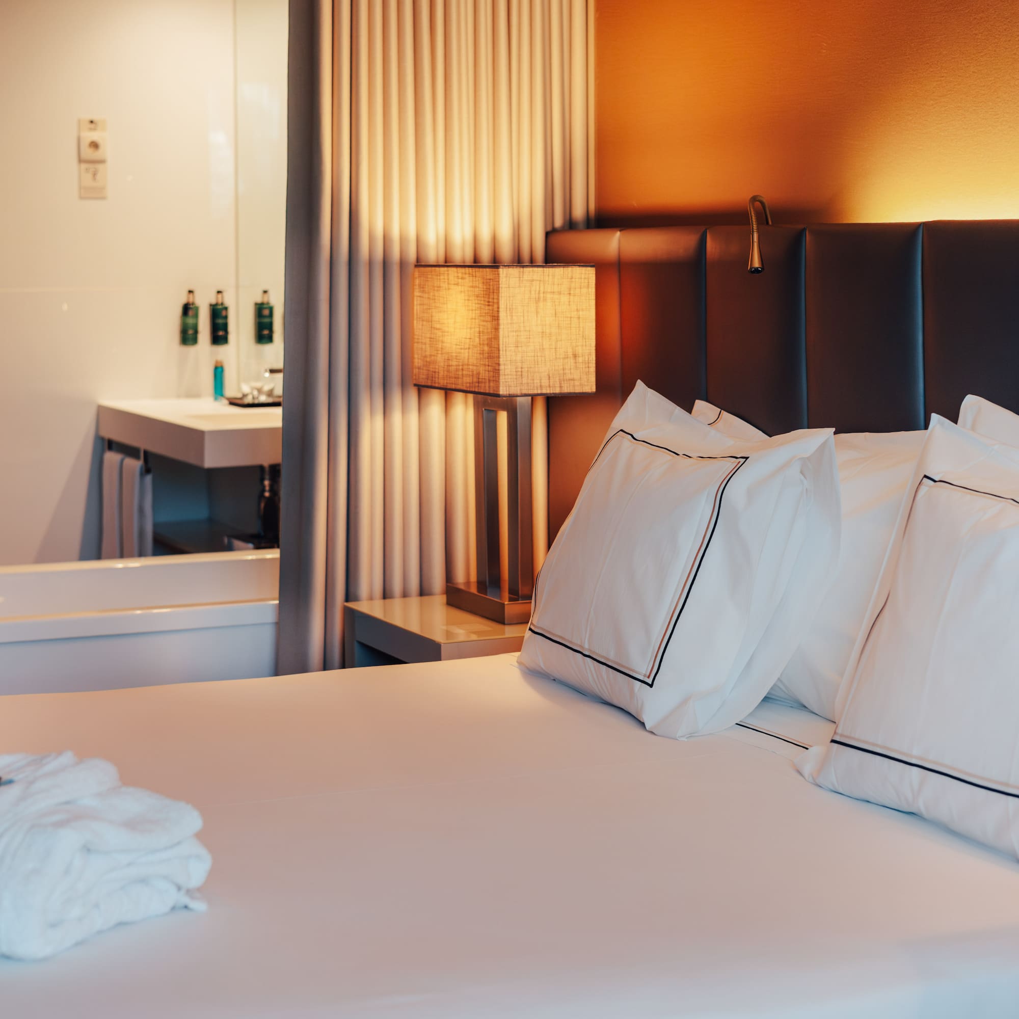 Elegant Meliá hotel room with bed, warm lamp, robes, and visible bathtub.