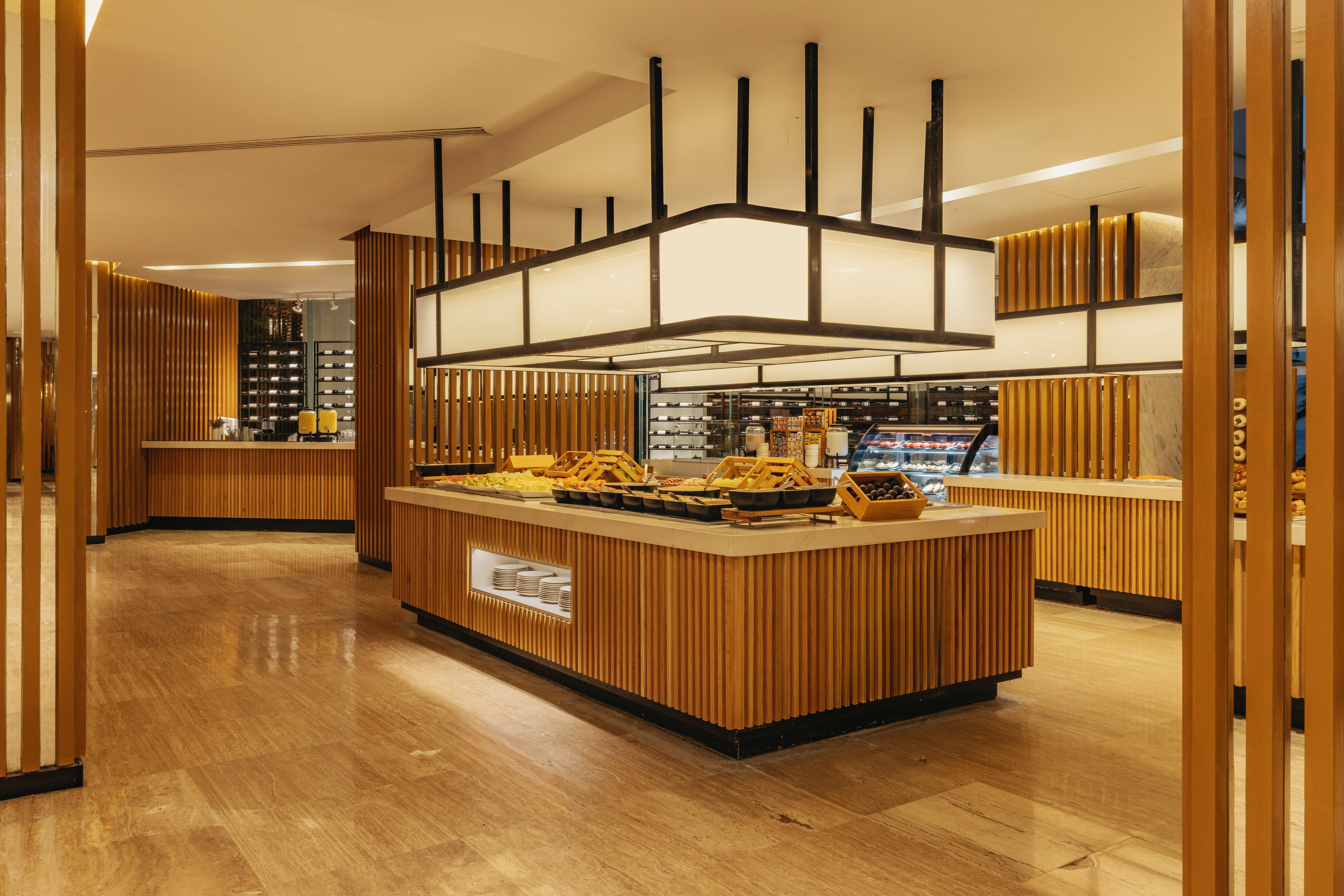 Modern hotel buffet with diverse food on wooden counters, warm lighting.