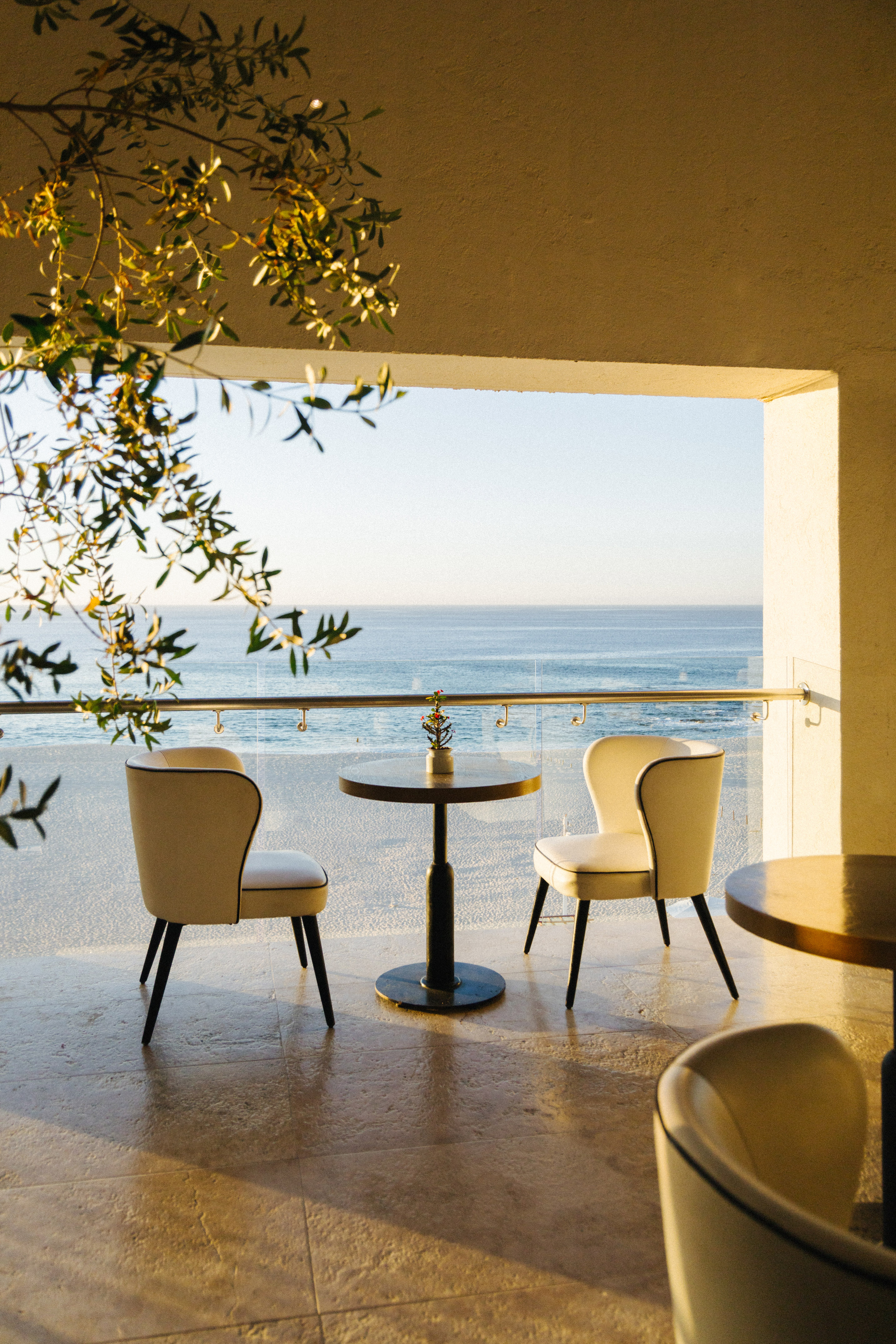Coastal balcony with modern chairs, table, and ocean view at golden hour.
