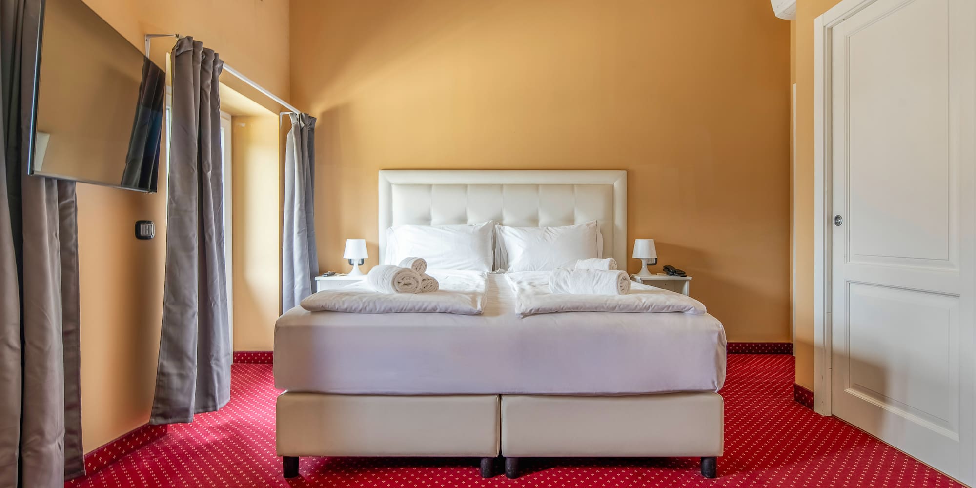 Hotel bedroom with white double bed, red patterned carpet, and gold walls.