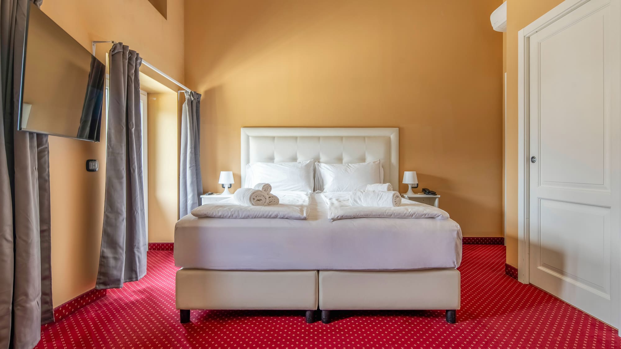 Hotel bedroom with white double bed, red patterned carpet, and gold walls.
