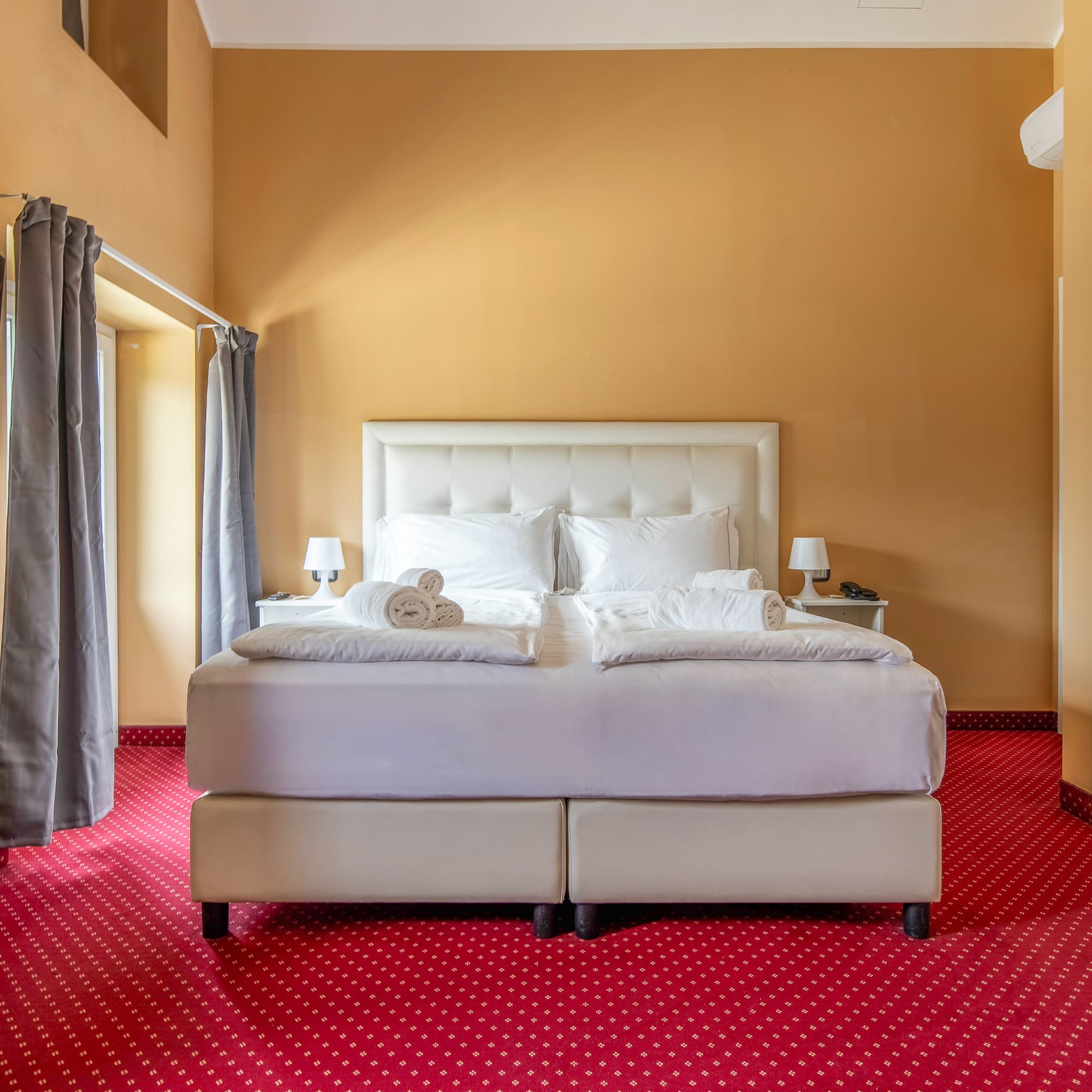 Hotel bedroom with white double bed, red patterned carpet, and gold walls.