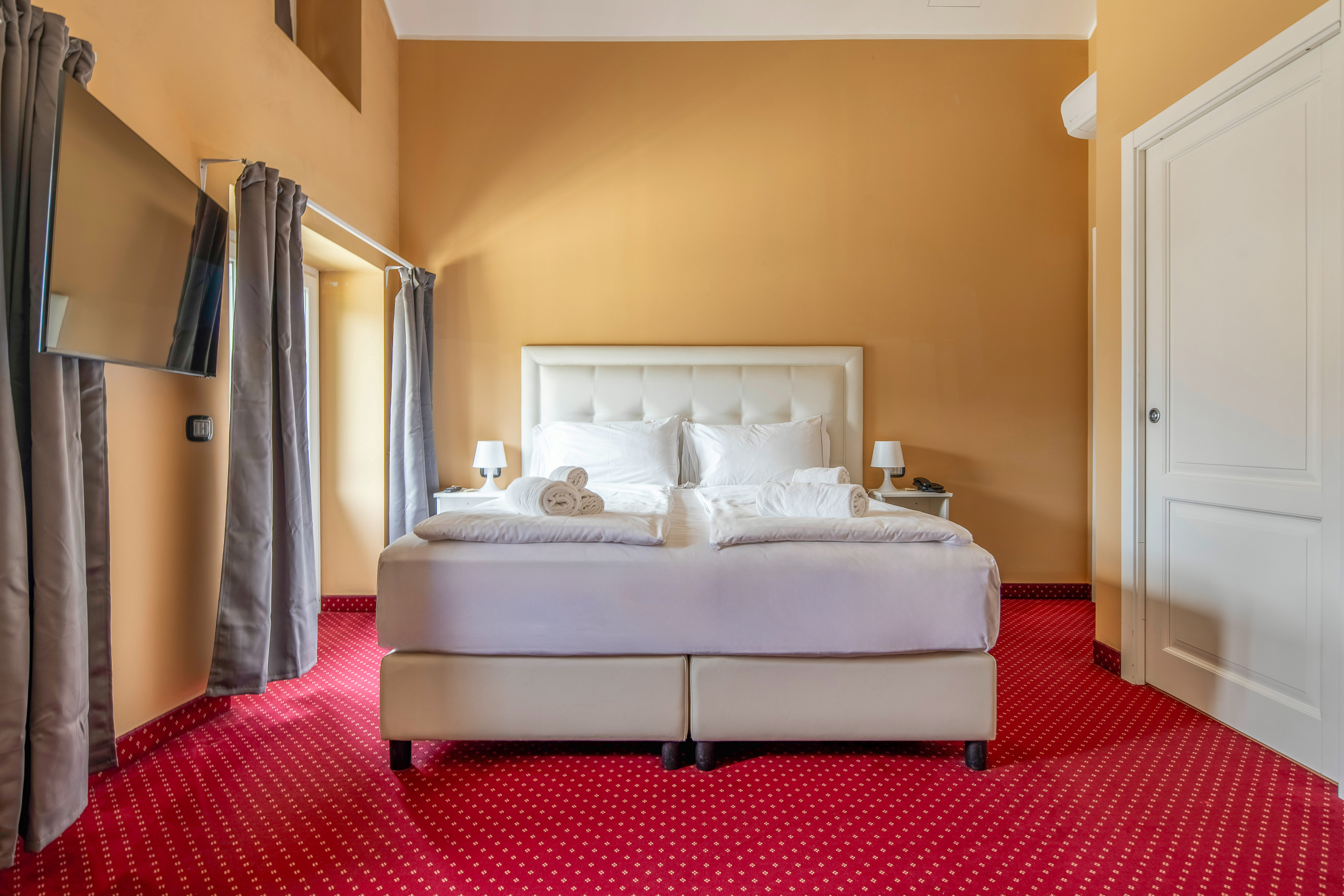 Hotel bedroom with white double bed, red patterned carpet, and gold walls.
