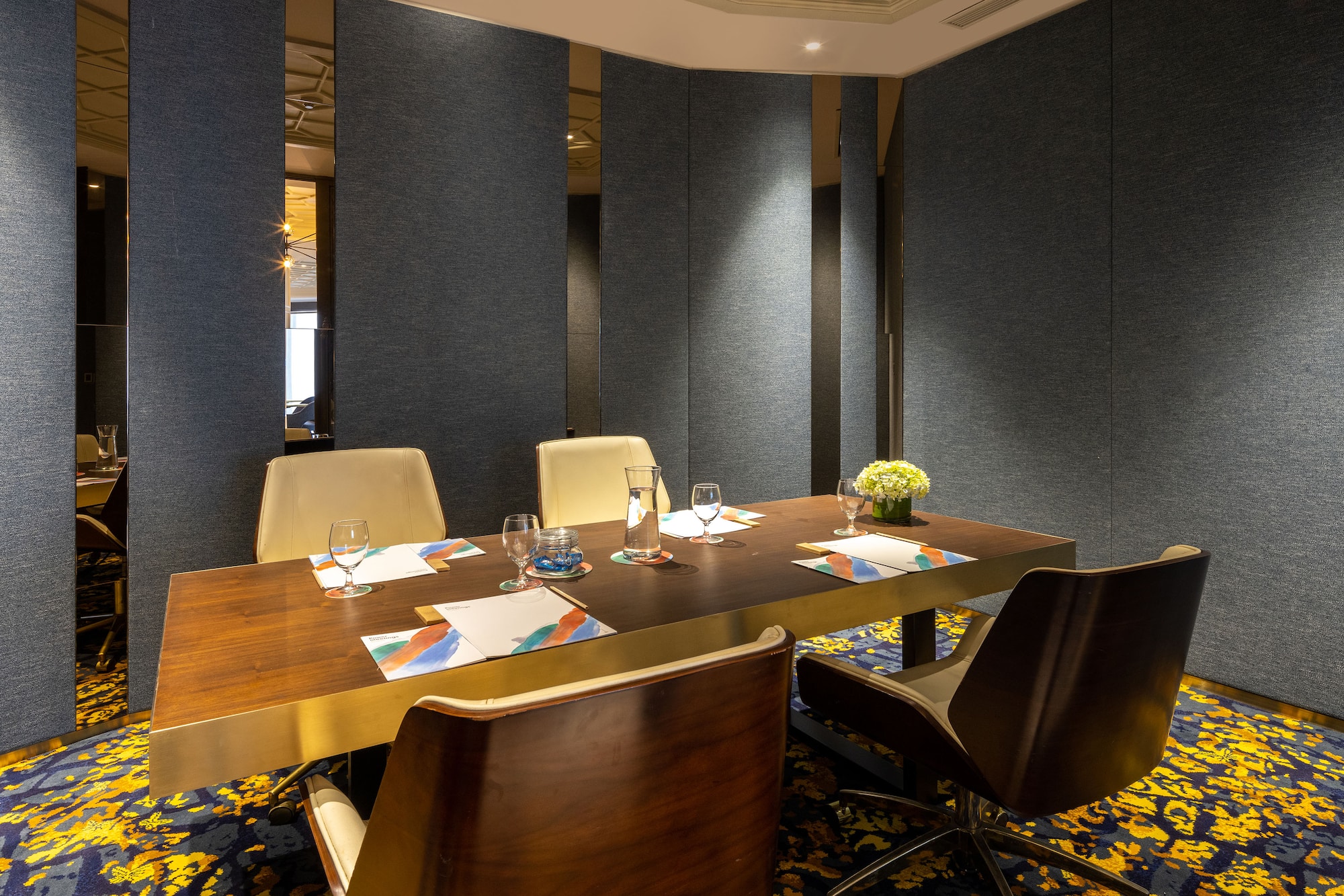 Modern meeting room, dark wood table, chairs, vibrant patterned carpet.