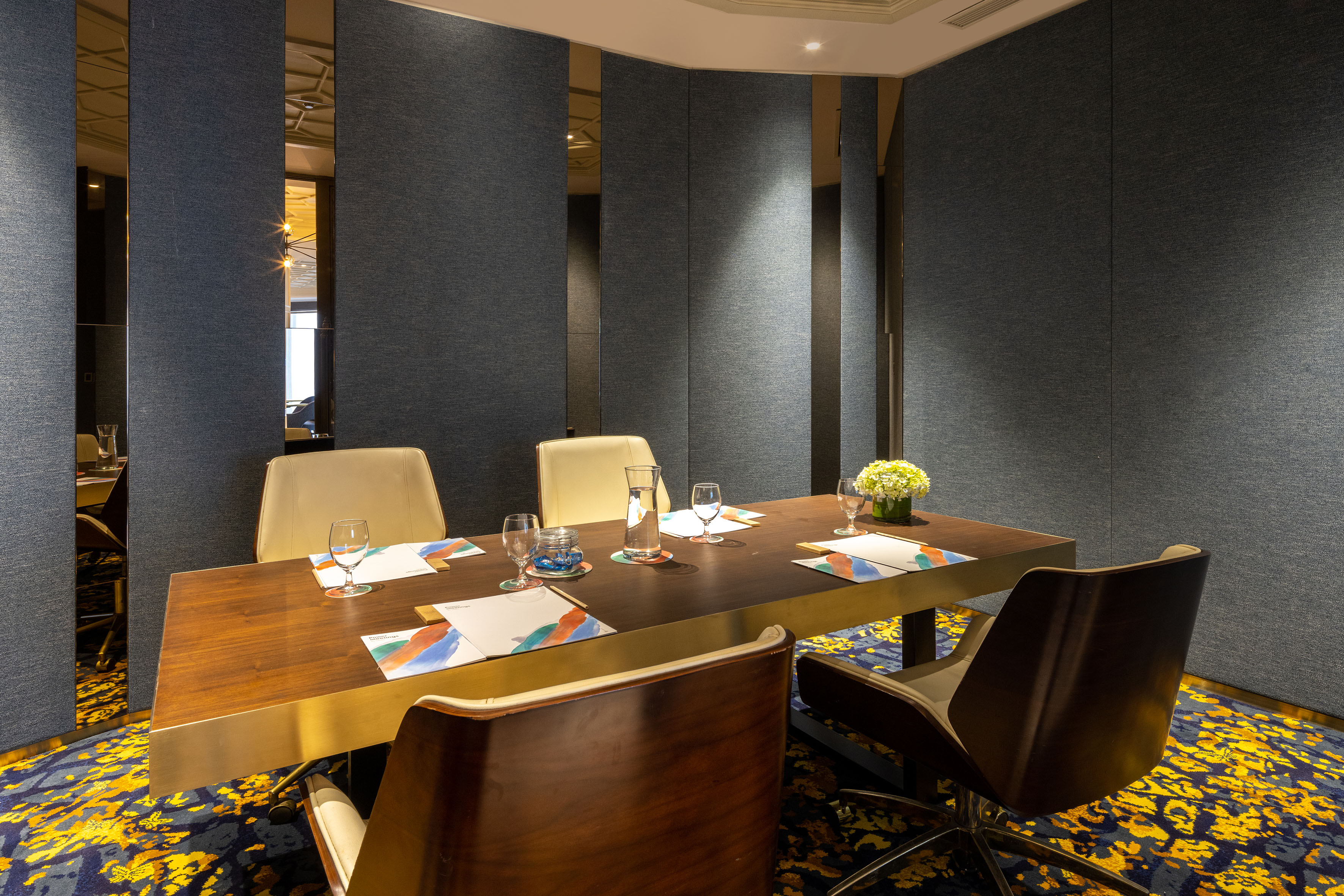 Modern meeting room, dark wood table, chairs, vibrant patterned carpet.
