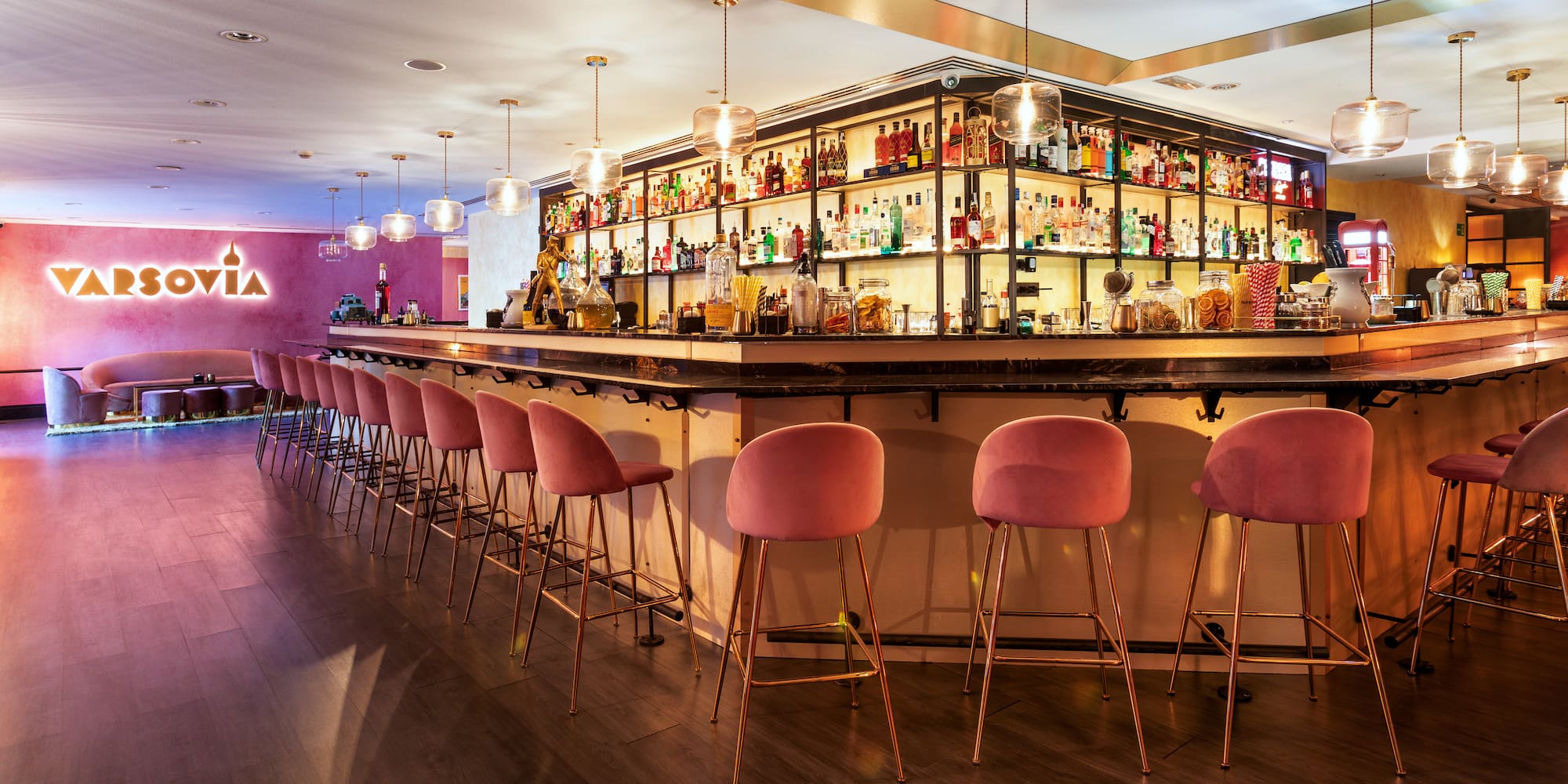 a bar with pink chairs and shelves with bottles