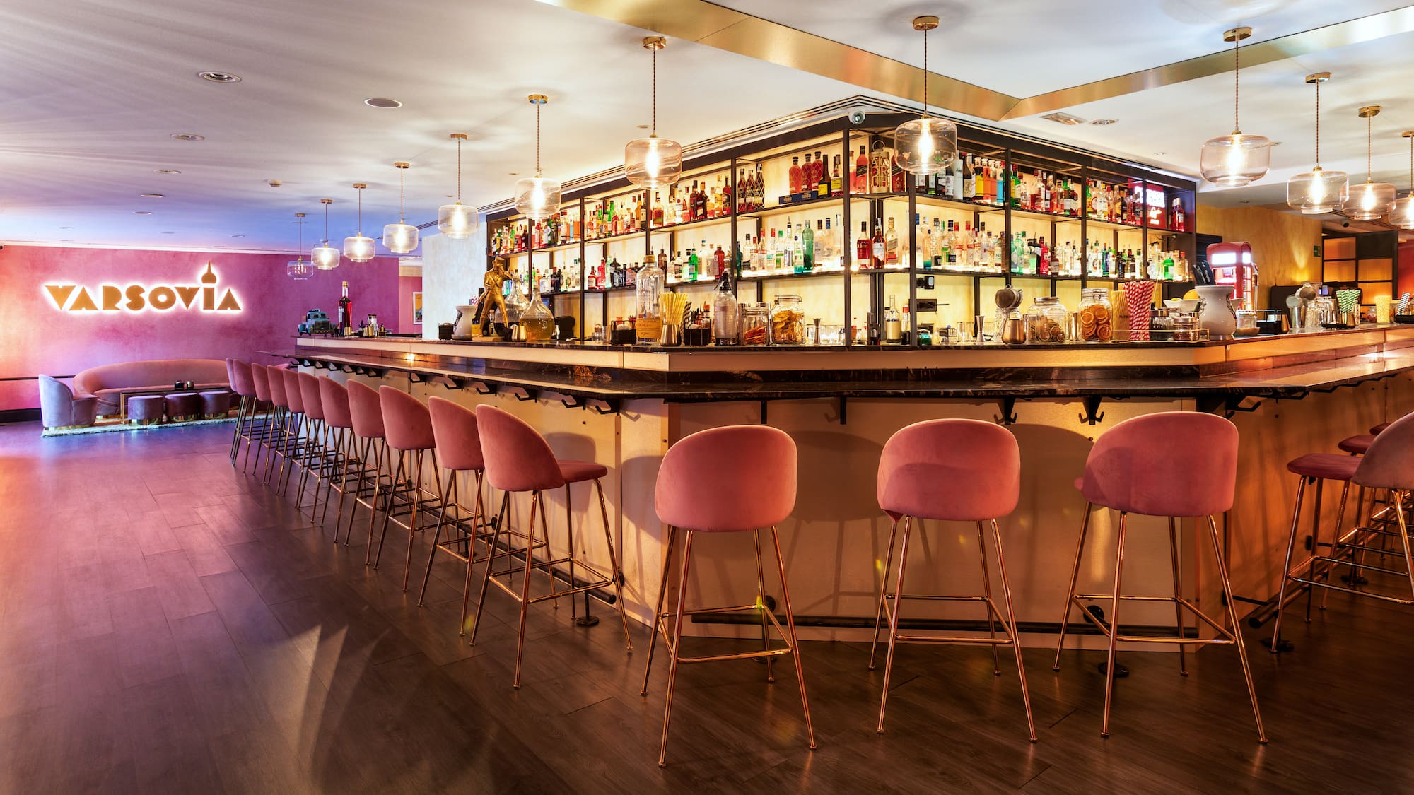 a bar with pink chairs and shelves with bottles