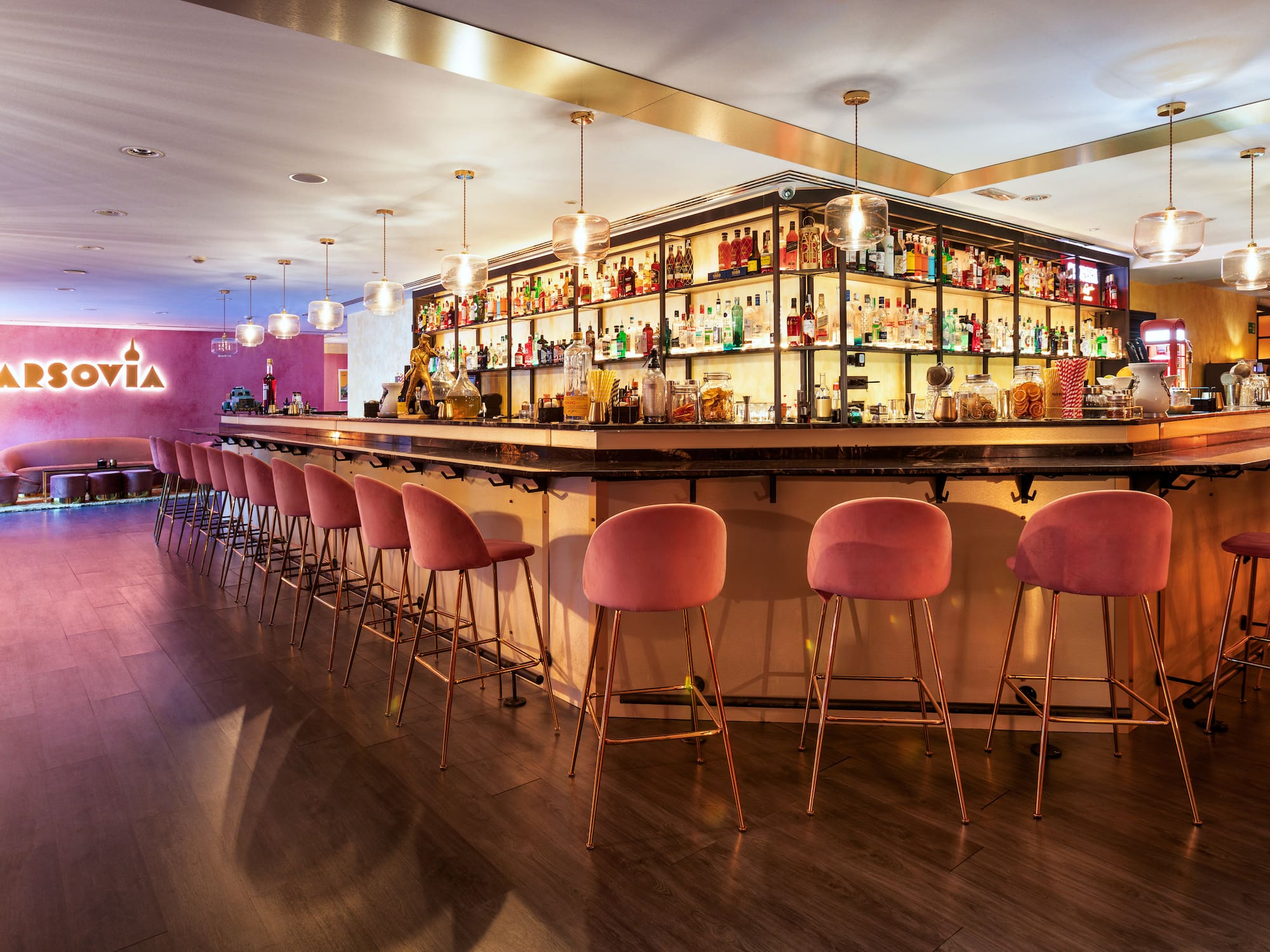 a bar with pink chairs and shelves with bottles