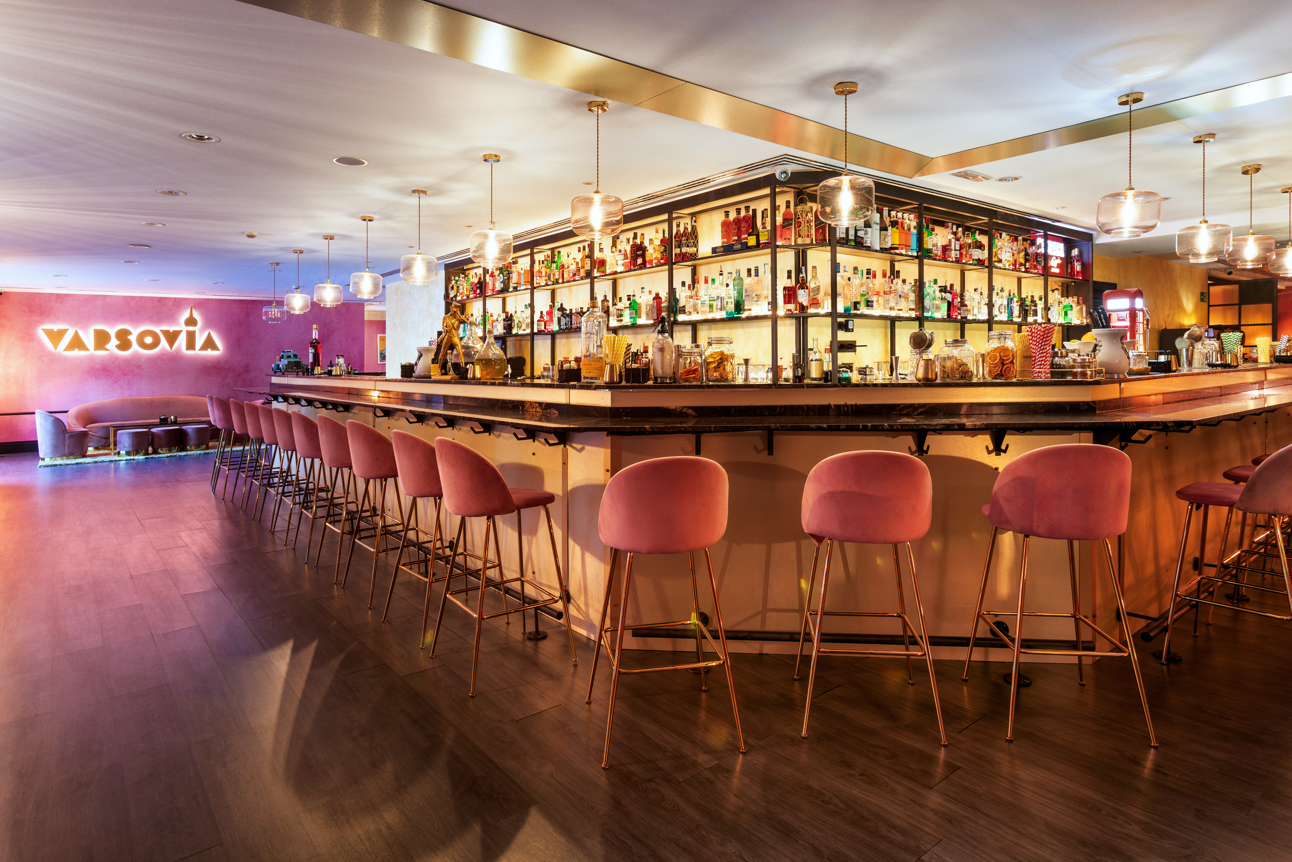 a bar with pink chairs and shelves with bottles