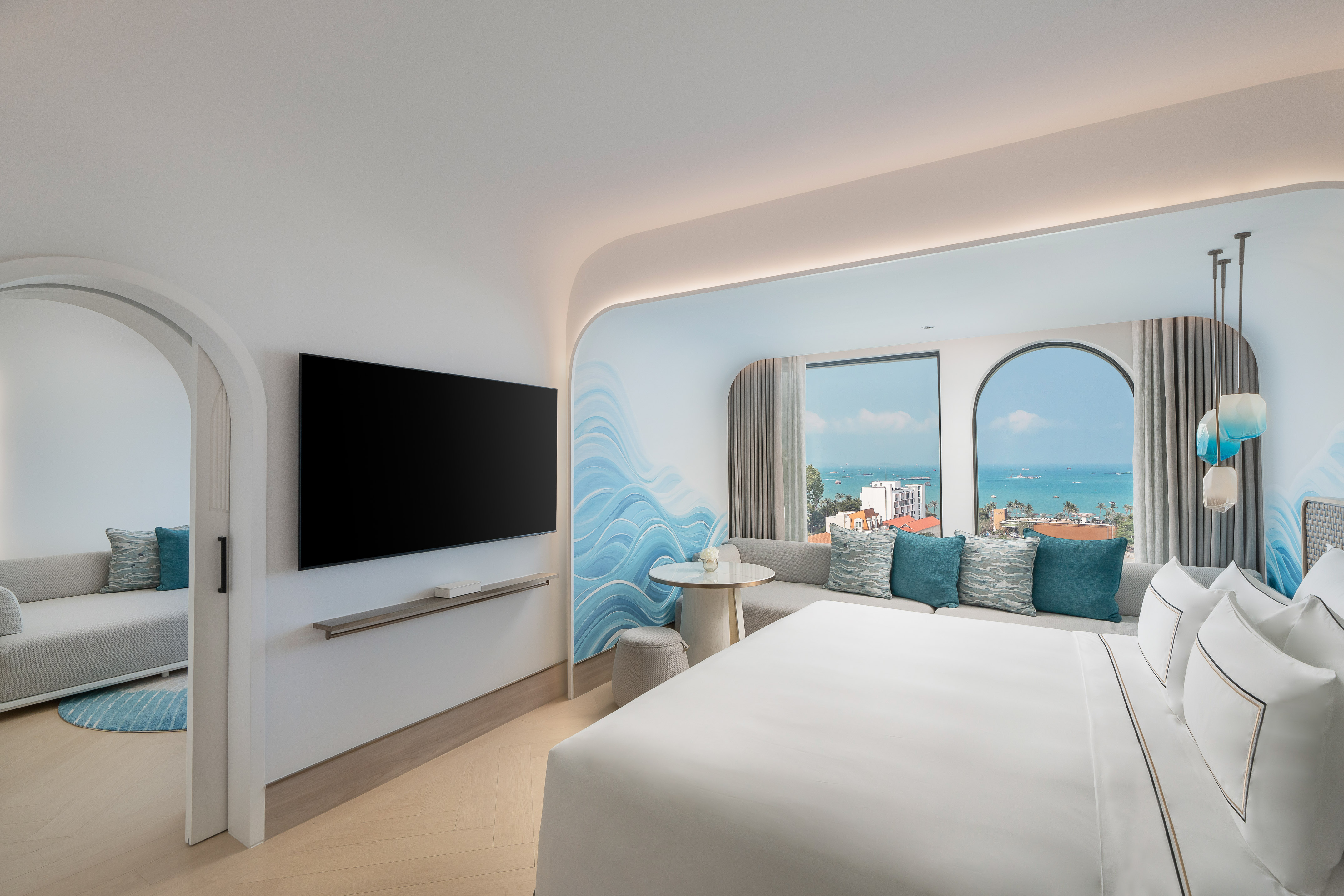 Contemporary hotel room with ocean view, bed, sofa, and blue wave accent wall.