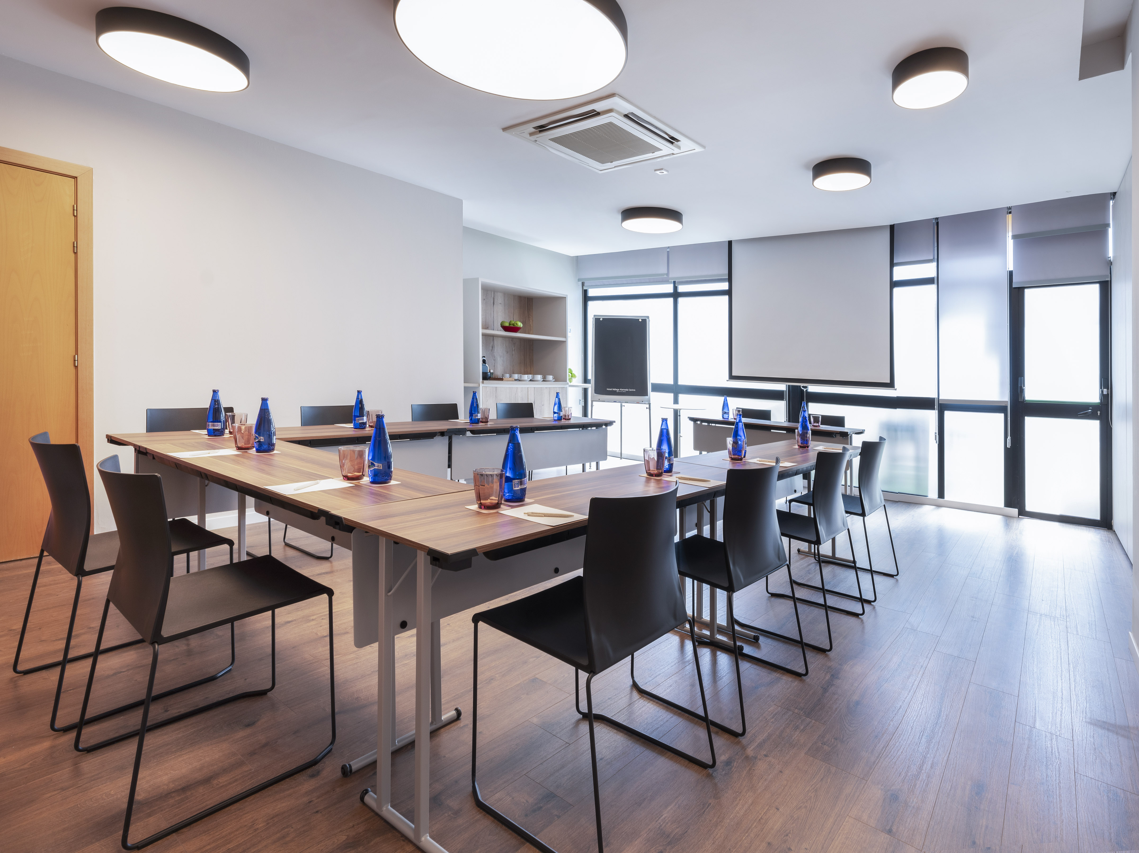 Modern conference room with U-shaped tables, black chairs, and projection screen.