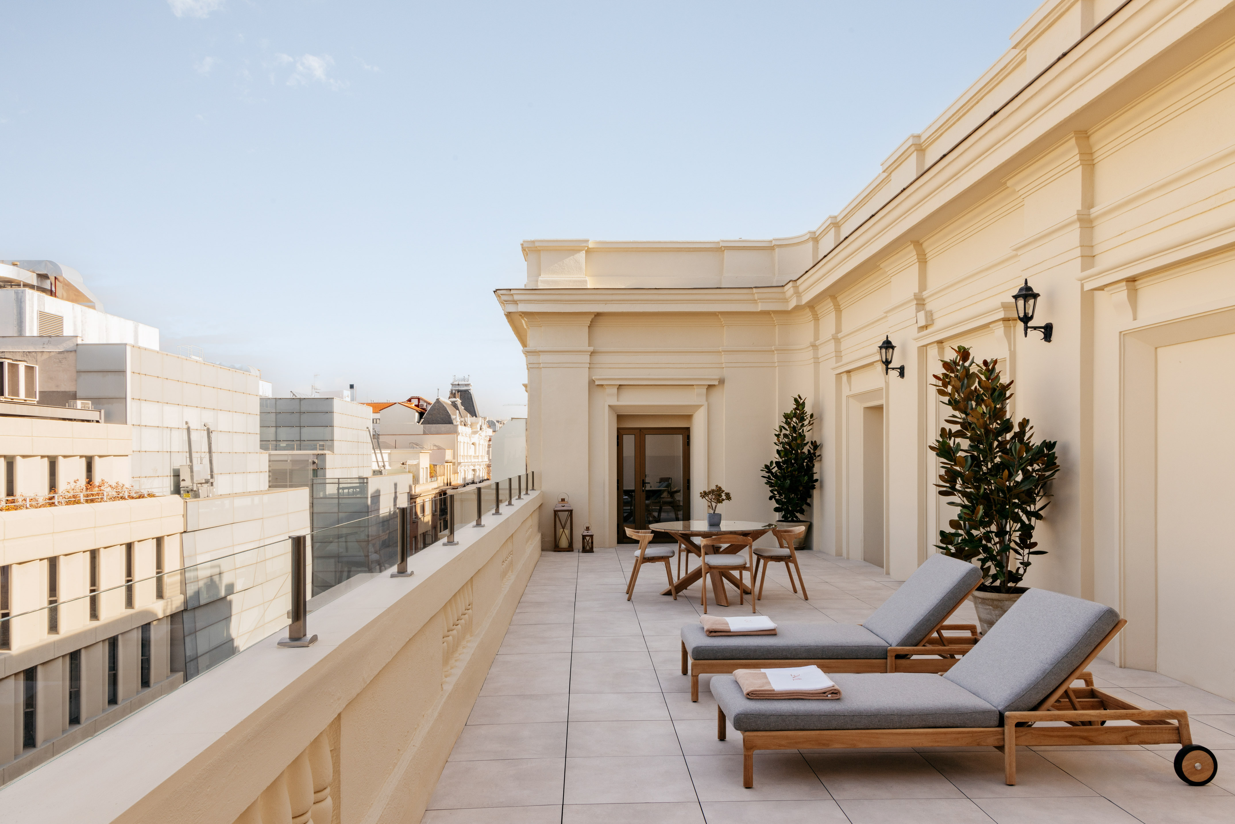 Luxury hotel rooftop terrace with lounge chairs, outdoor dining, and city view.