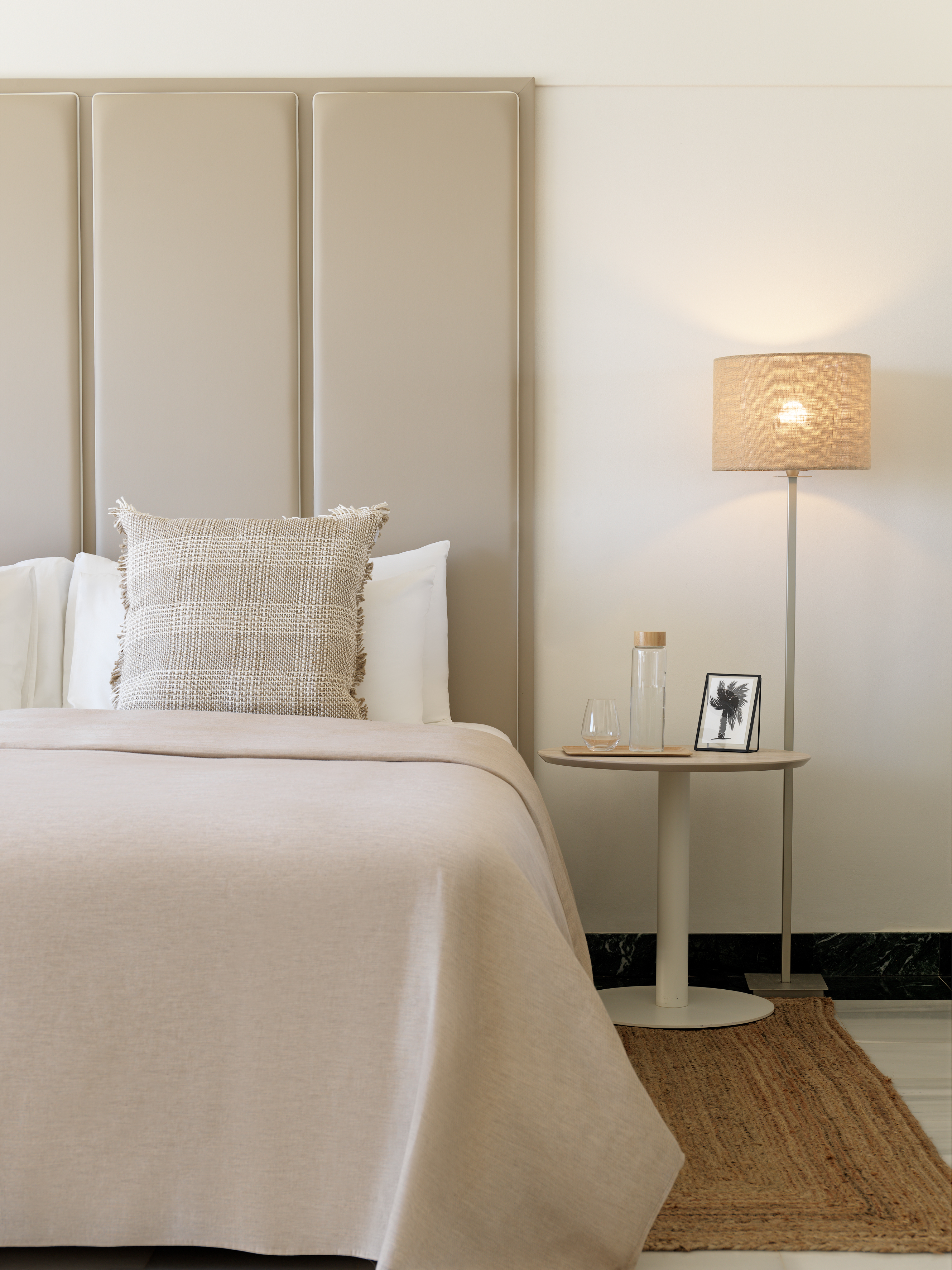 Neutral bedroom: beige bed, upholstered headboard, floor lamp, bedside table.