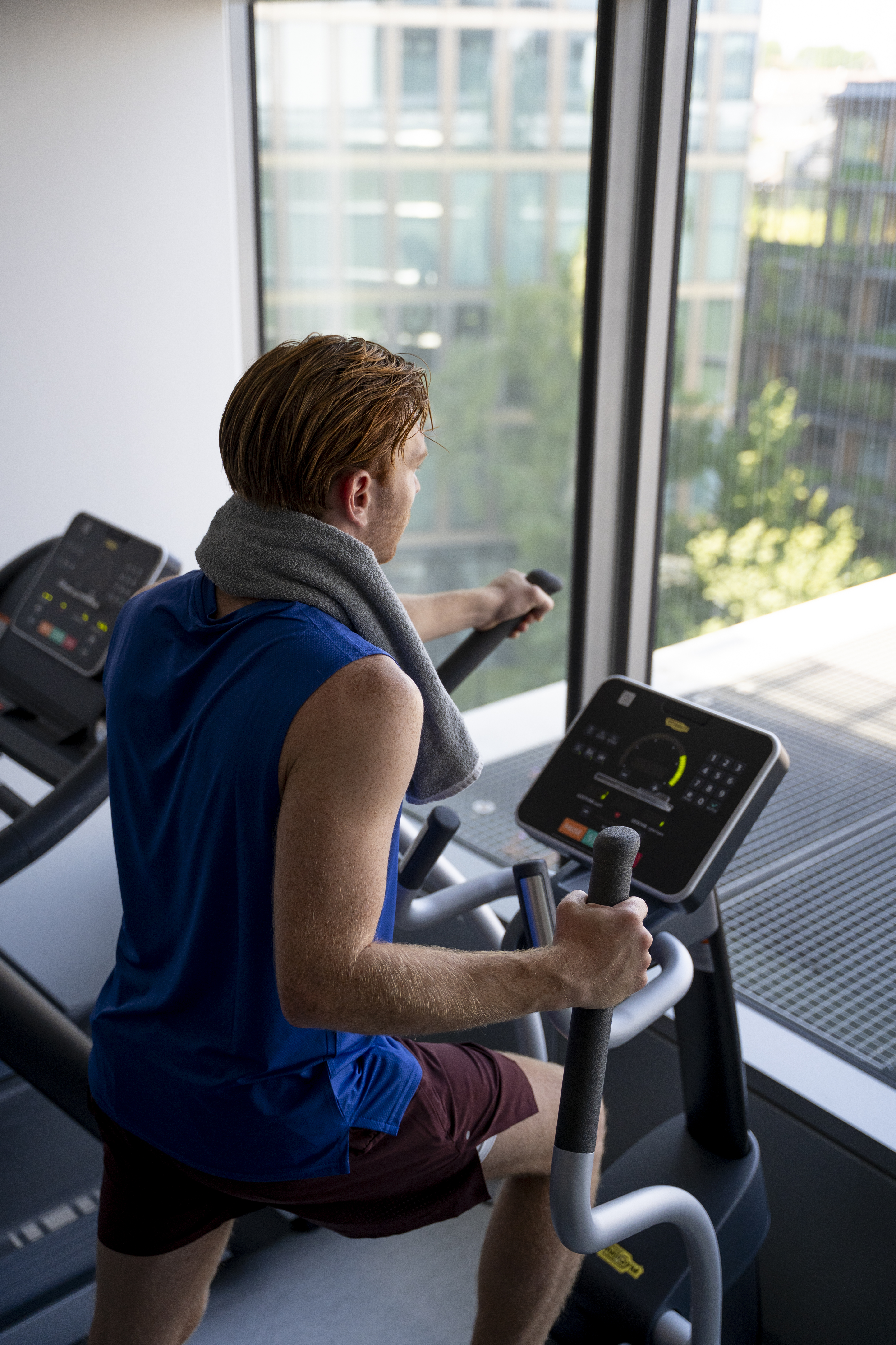 Man with towel on neck on elliptical machine in gym looking out window.