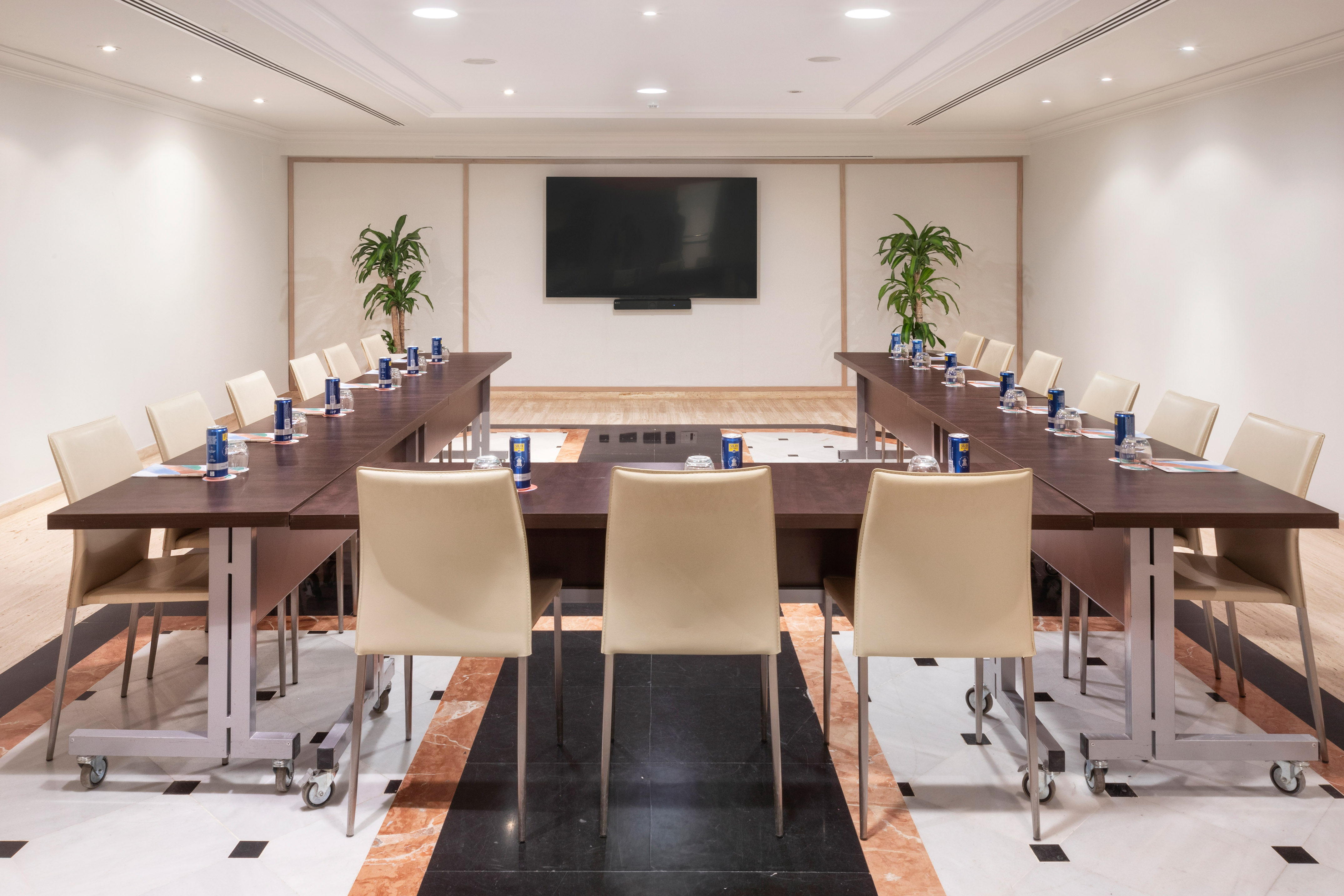 Modern U-shaped meeting room with large presentation screen and beige seating.