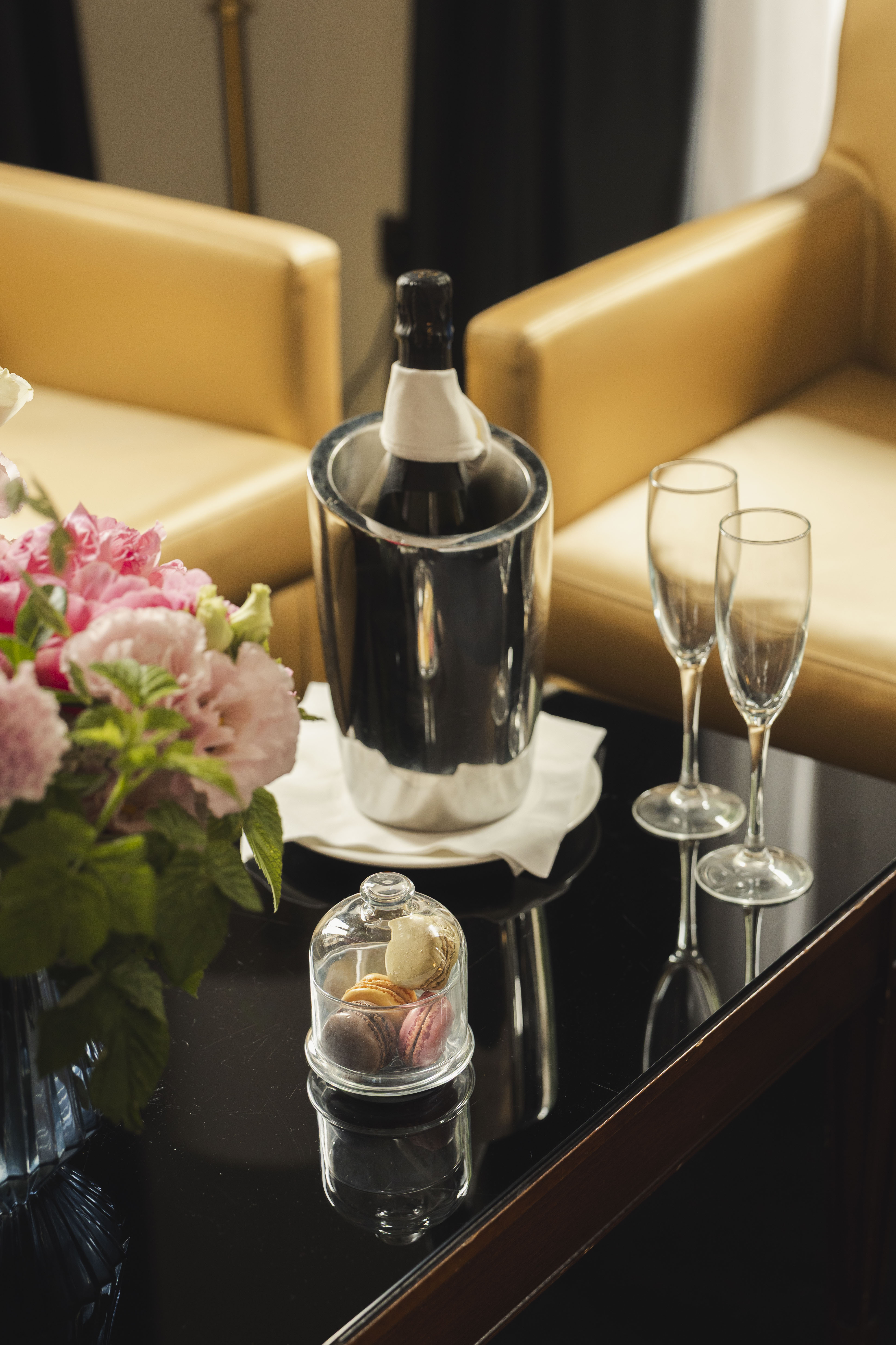 Luxury hotel amenities: champagne, flutes, macarons, and flowers.