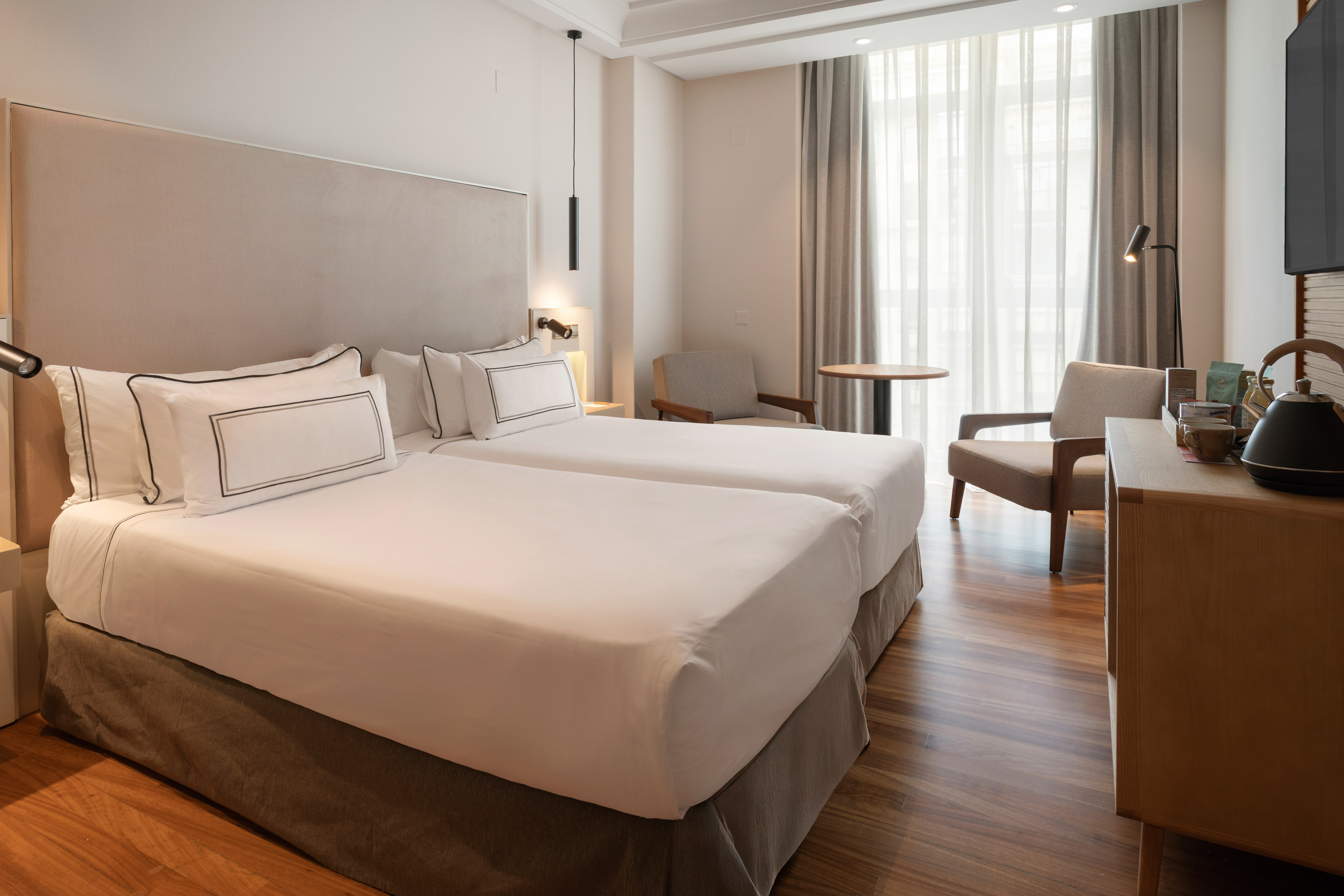 Elegant hotel guest room with twin beds, bright window, and wooden floors.