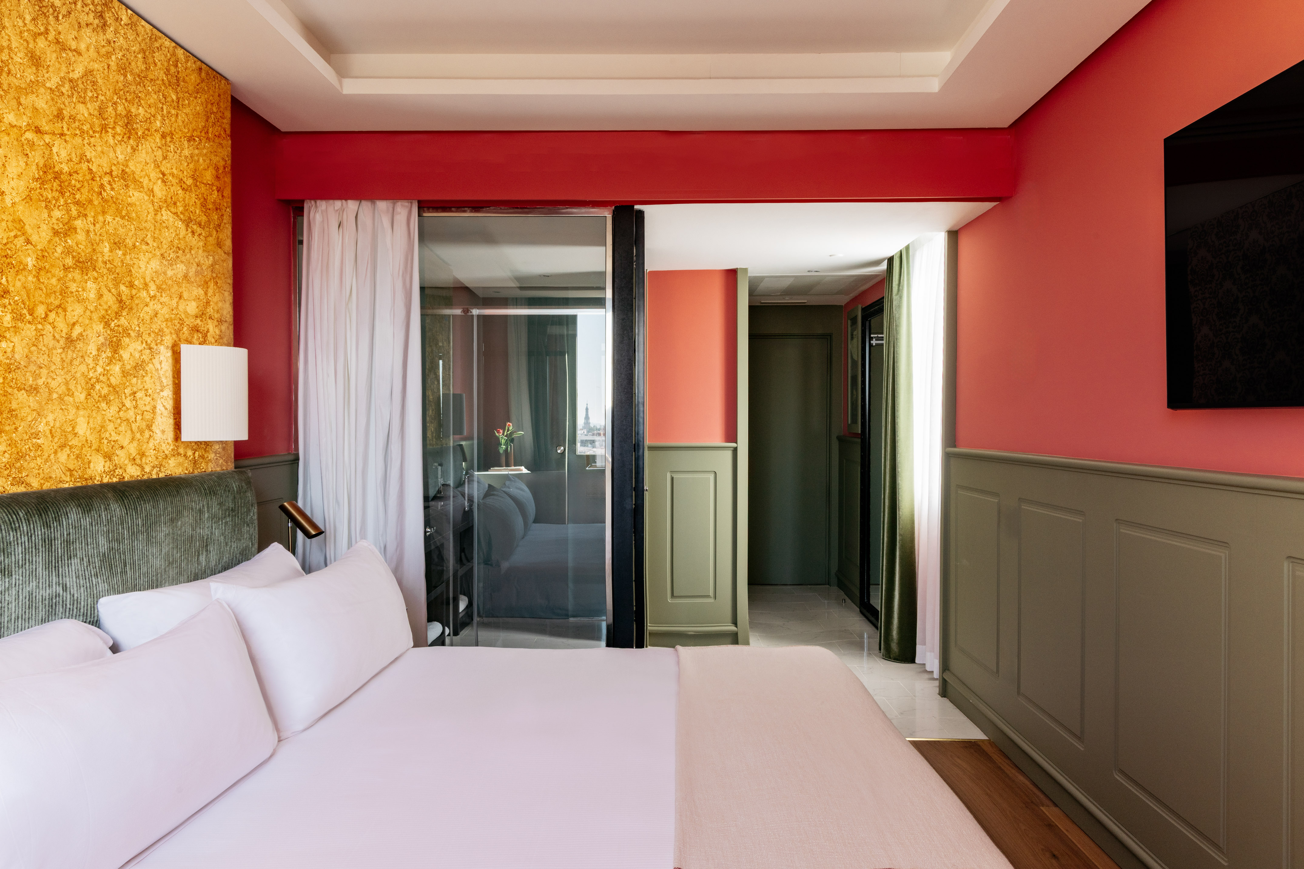 Modern hotel bedroom with gold accent wall, red ceiling, and glass partition.