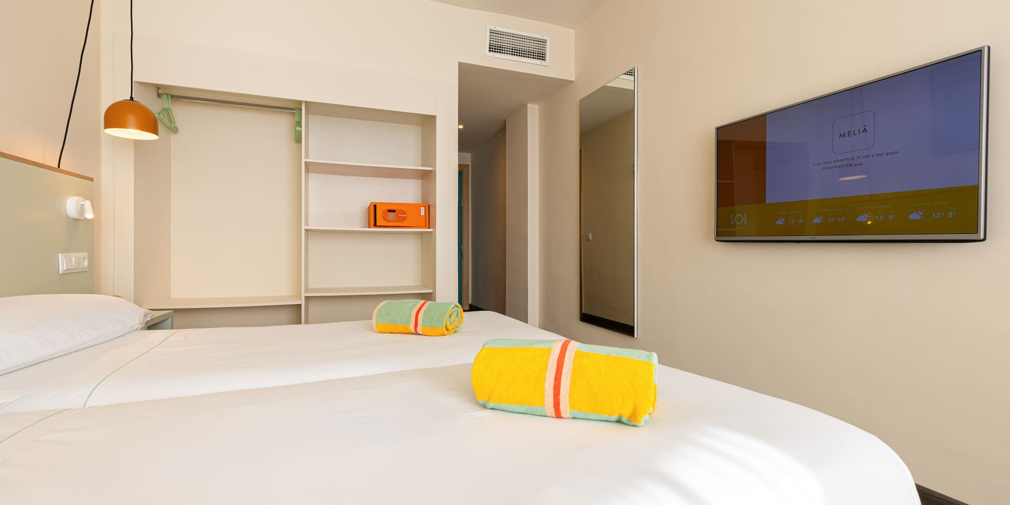 Melia hotel room with twin beds, colorful towels, wall TV, and open closet.
