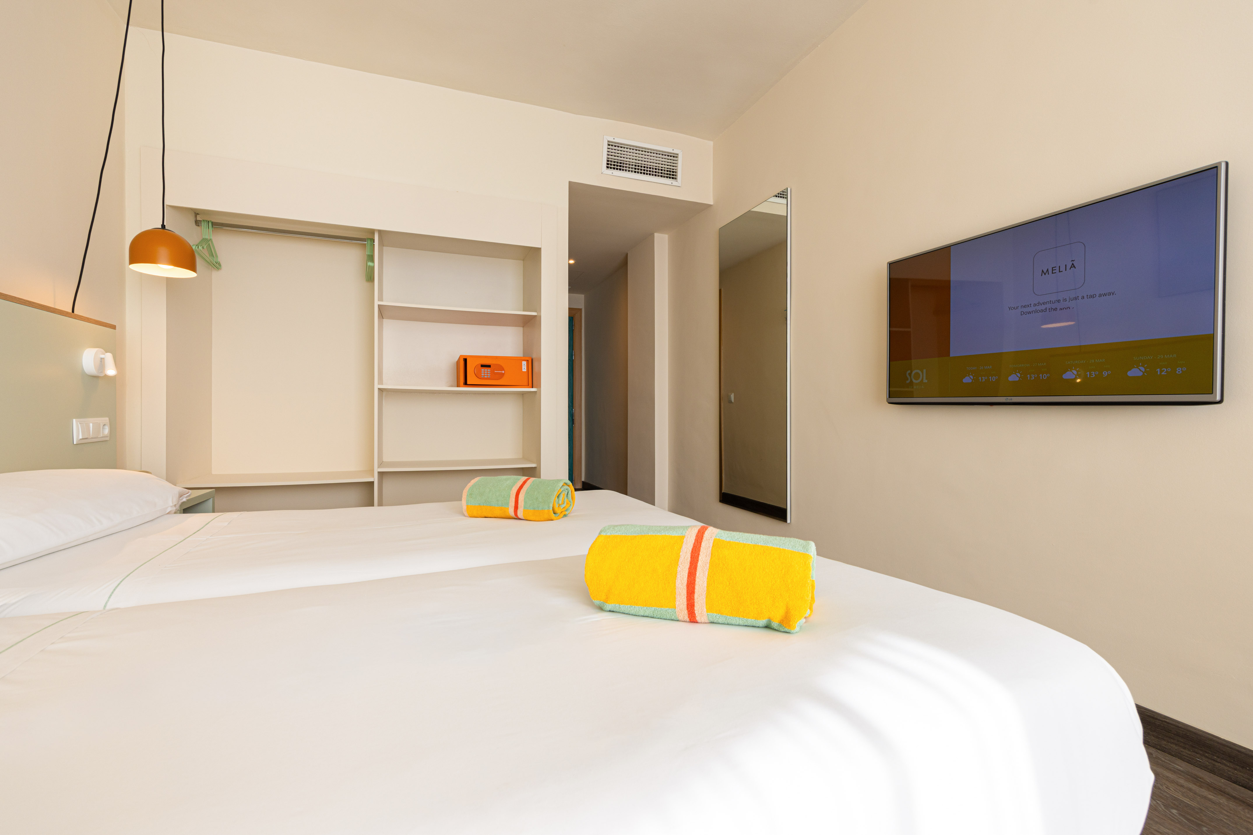 Melia hotel room with twin beds, colorful towels, wall TV, and open closet.