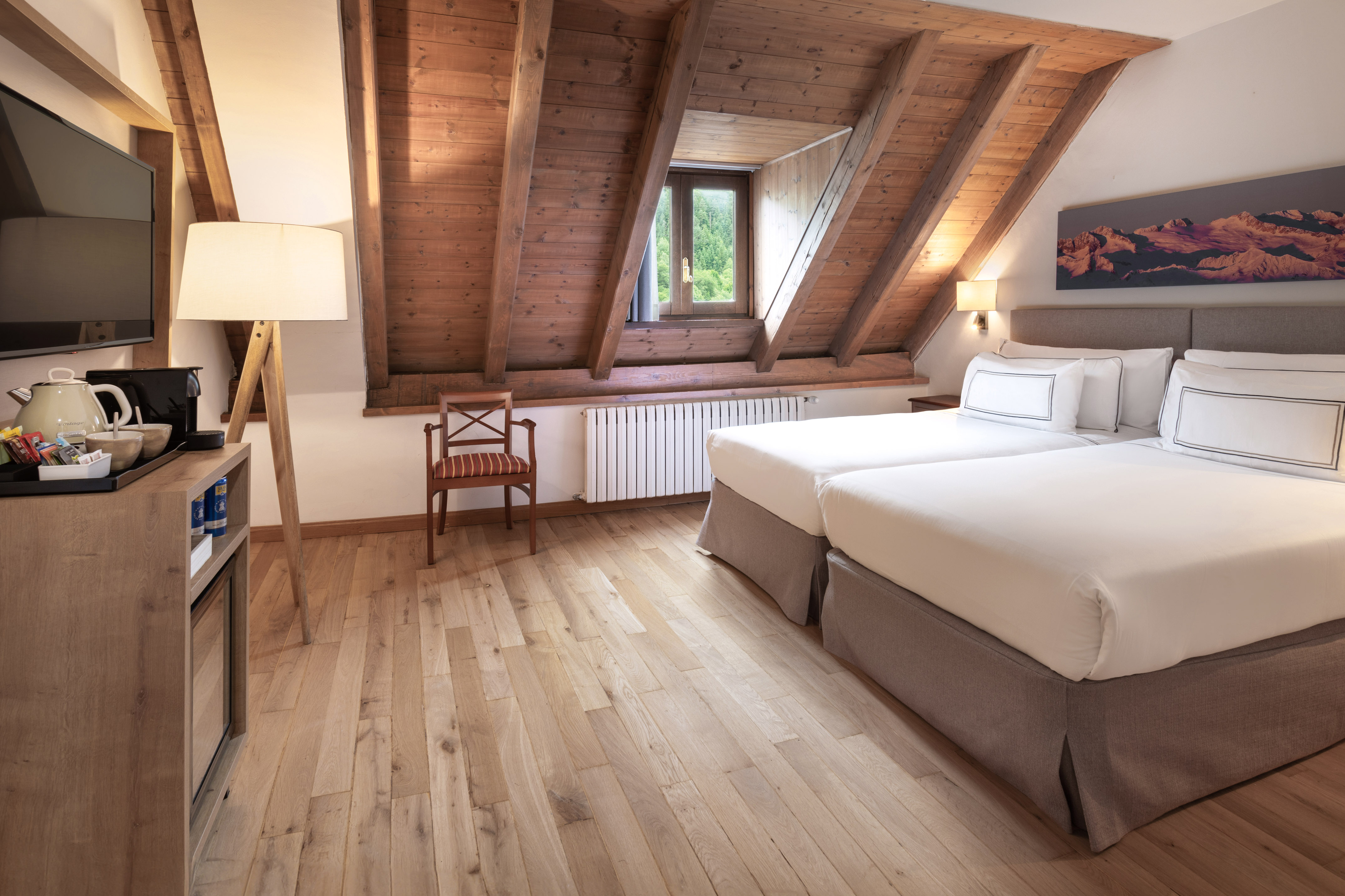 Attic hotel room with two beds, exposed wooden beams, and forest view window.