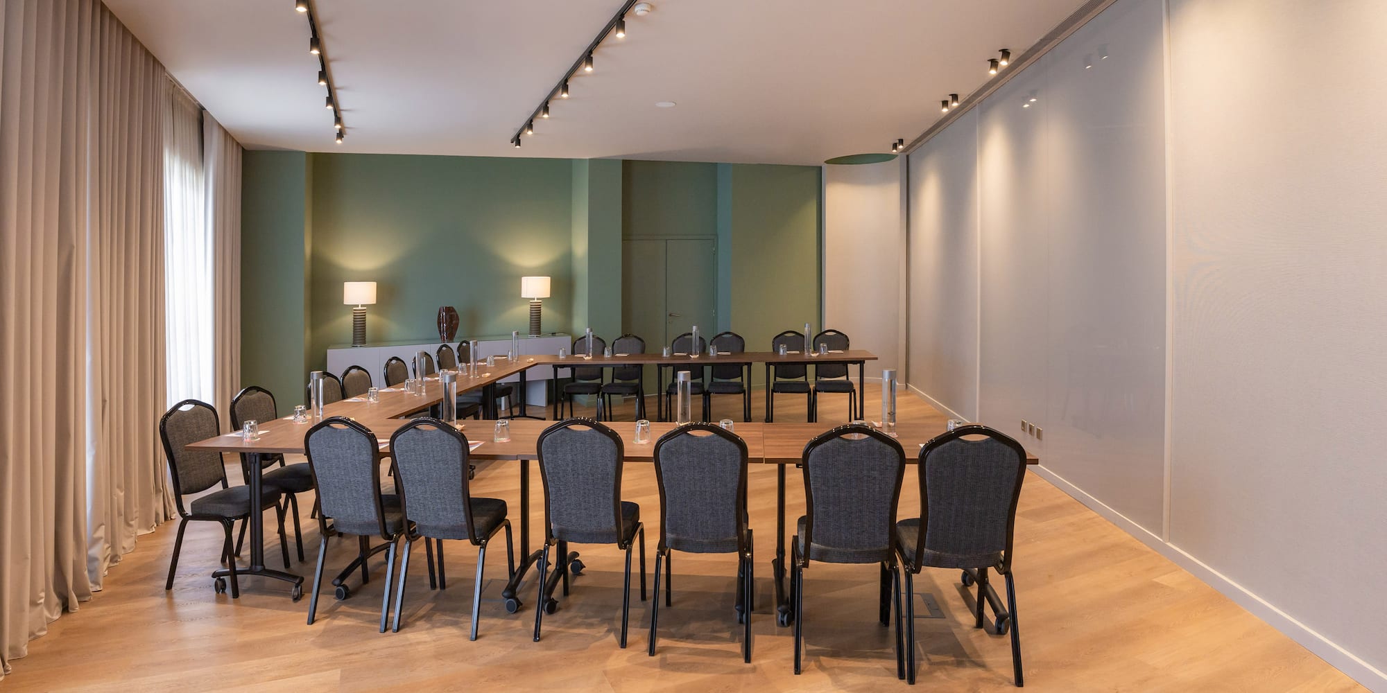 Modern conference room with U-shaped table setup, green walls, and wood floor.
