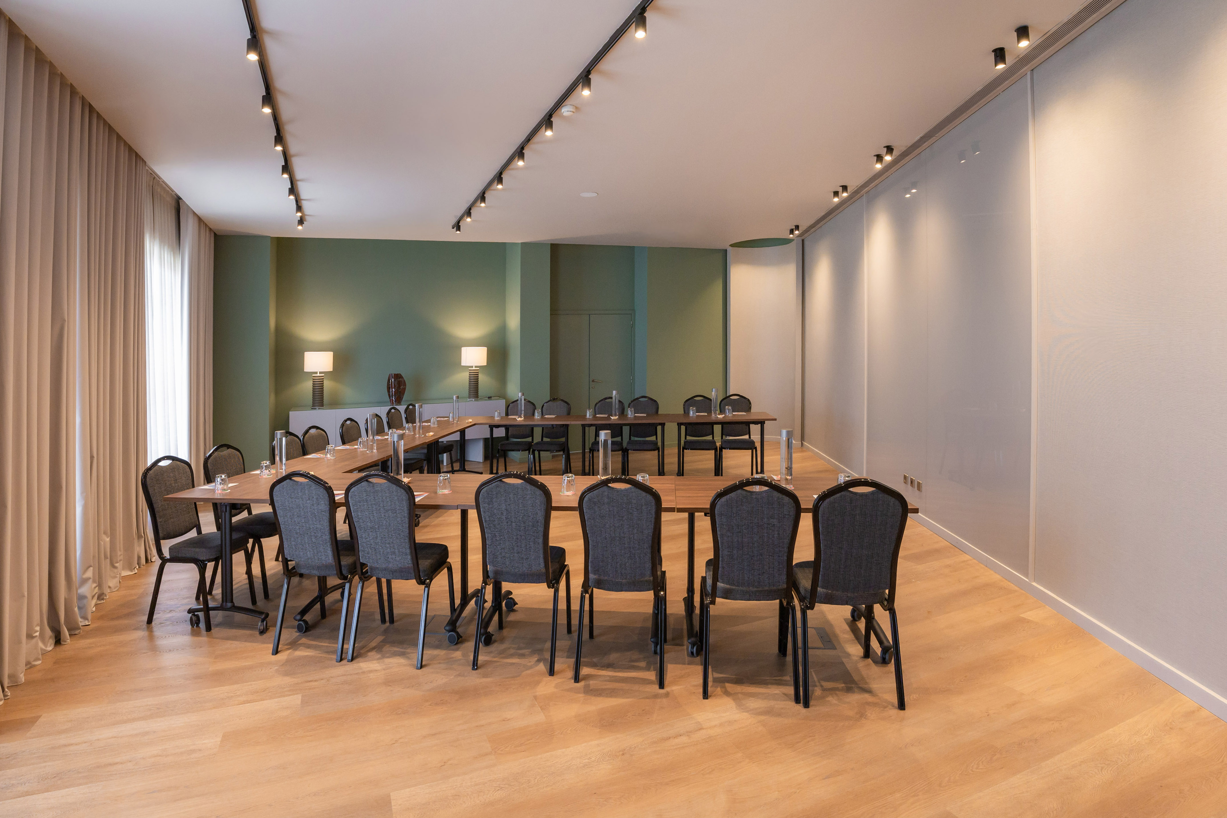 Modern conference room with U-shaped table setup, green walls, and wood floor.