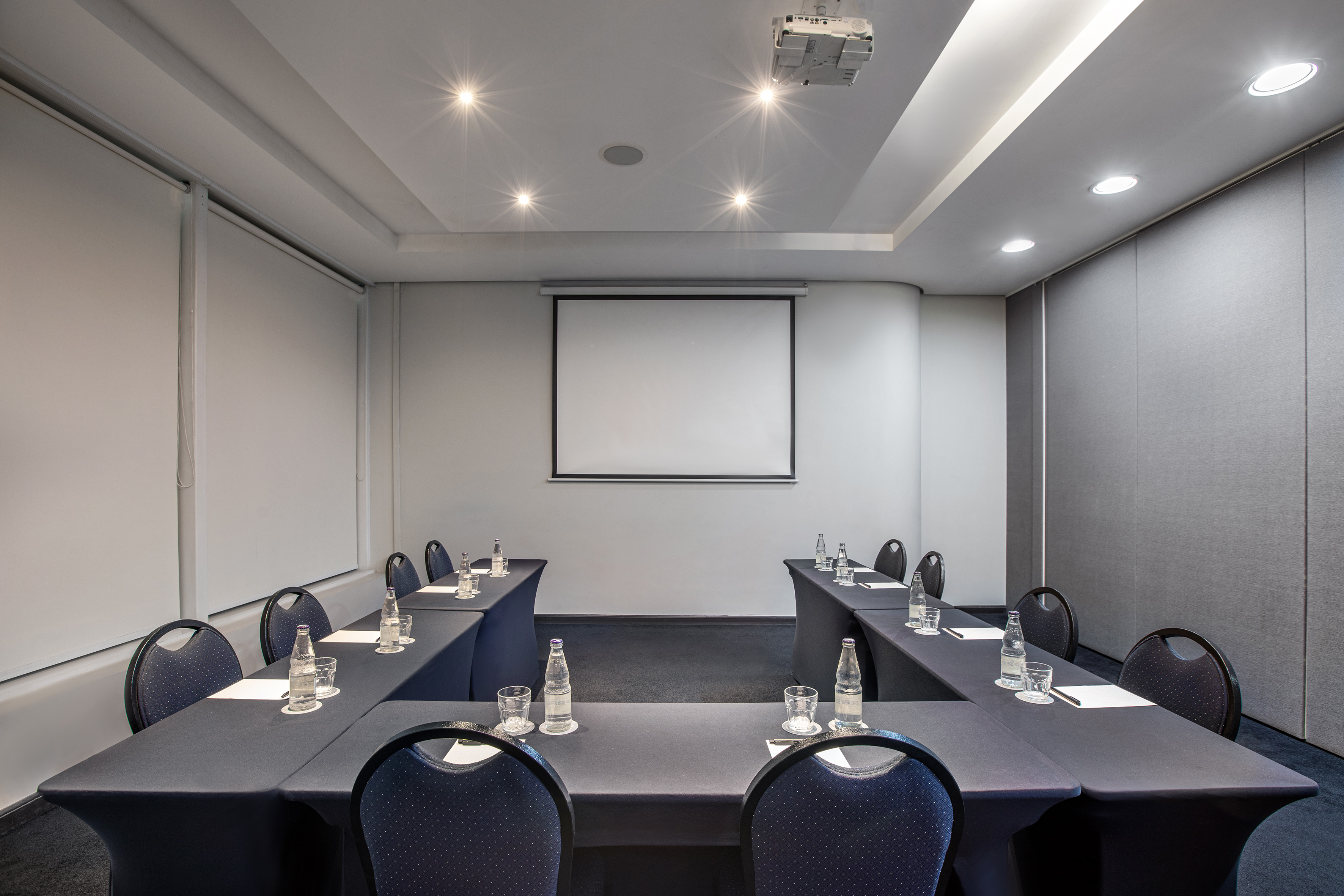 Modern conference room with projector screen, U-shaped table setup, and chairs.