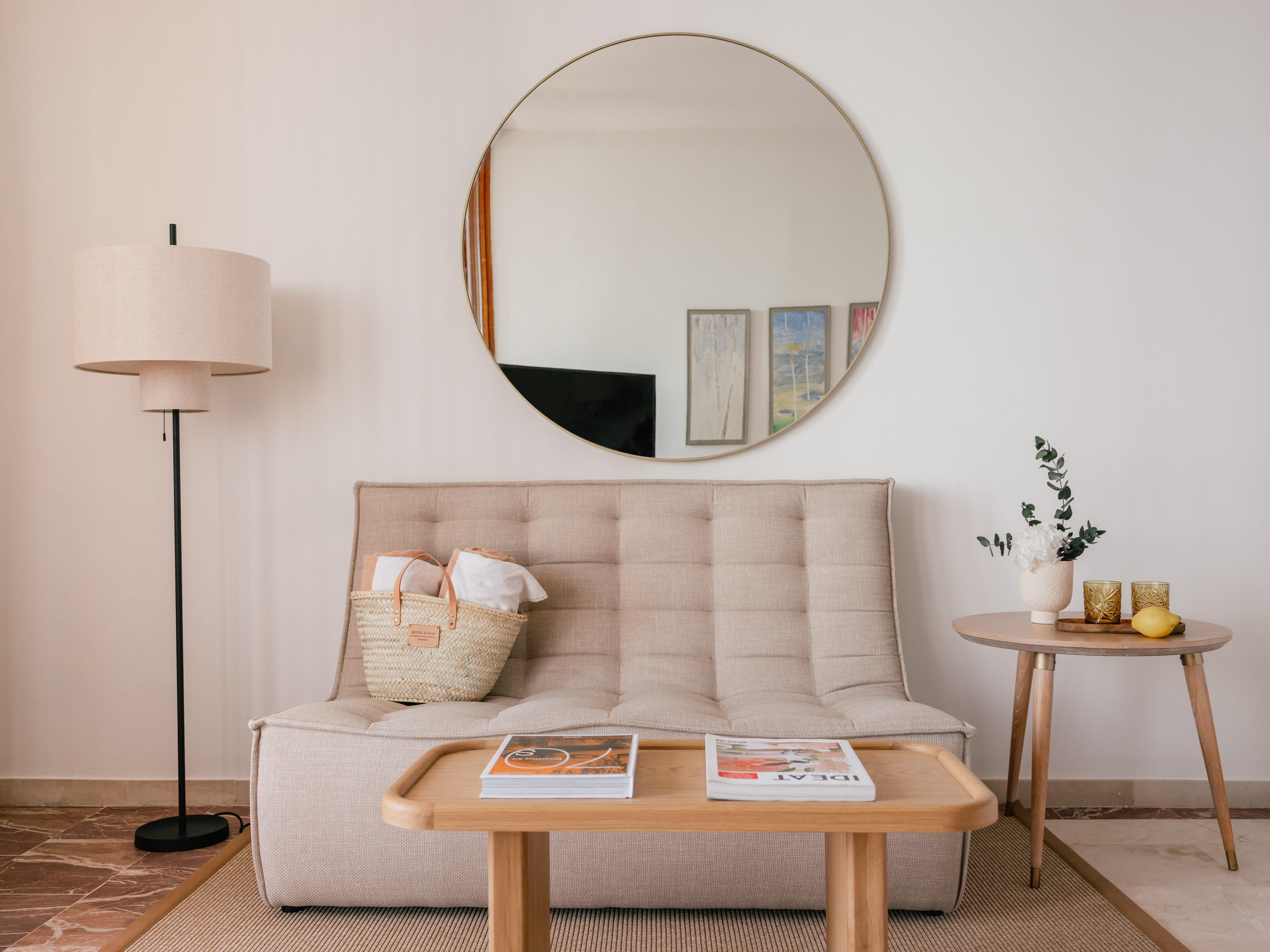 Modern living room with beige sofa, round mirror, and wood tables.