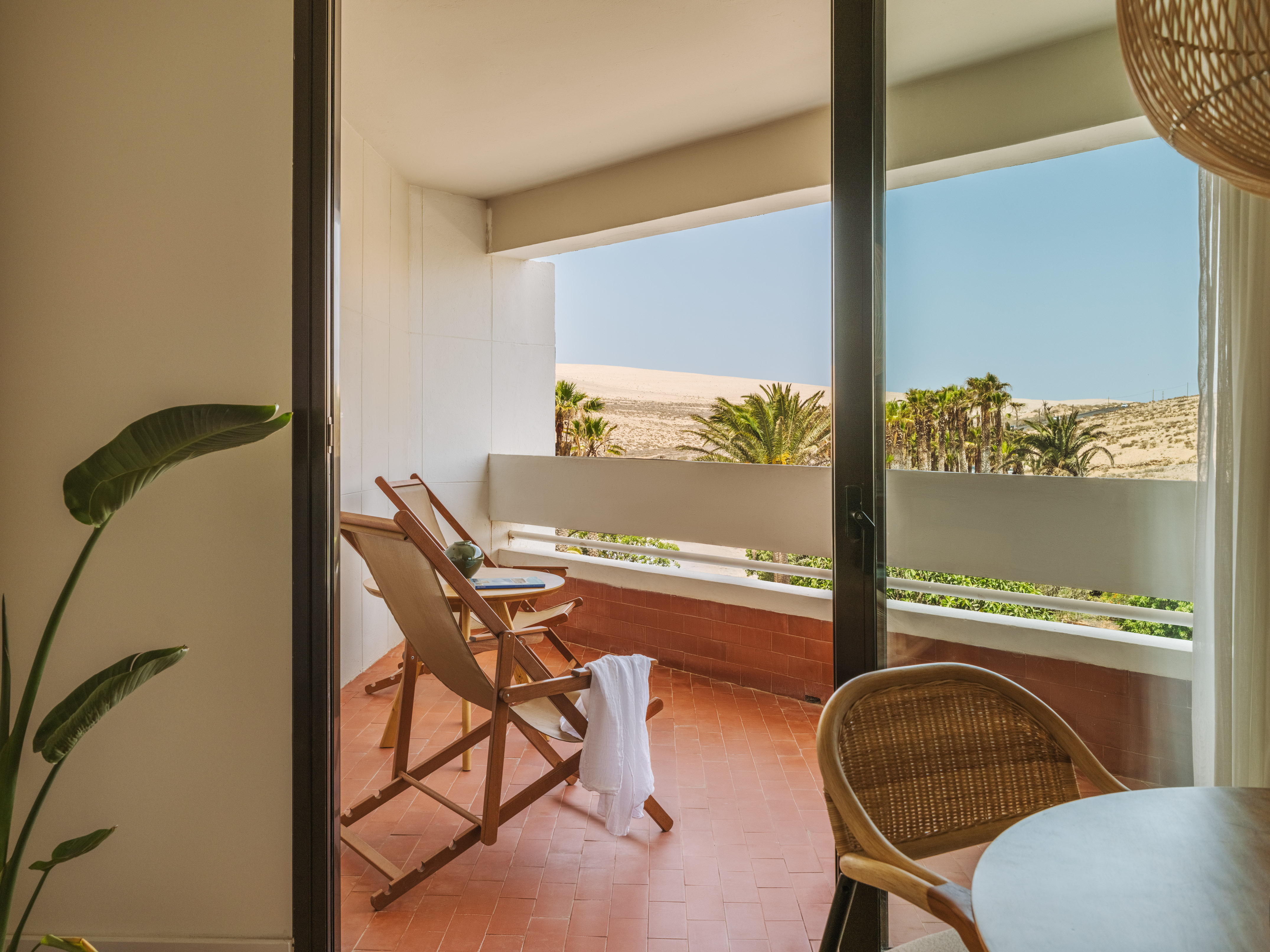 Hotel balcony with sand dunes, palm trees, and outdoor seating.