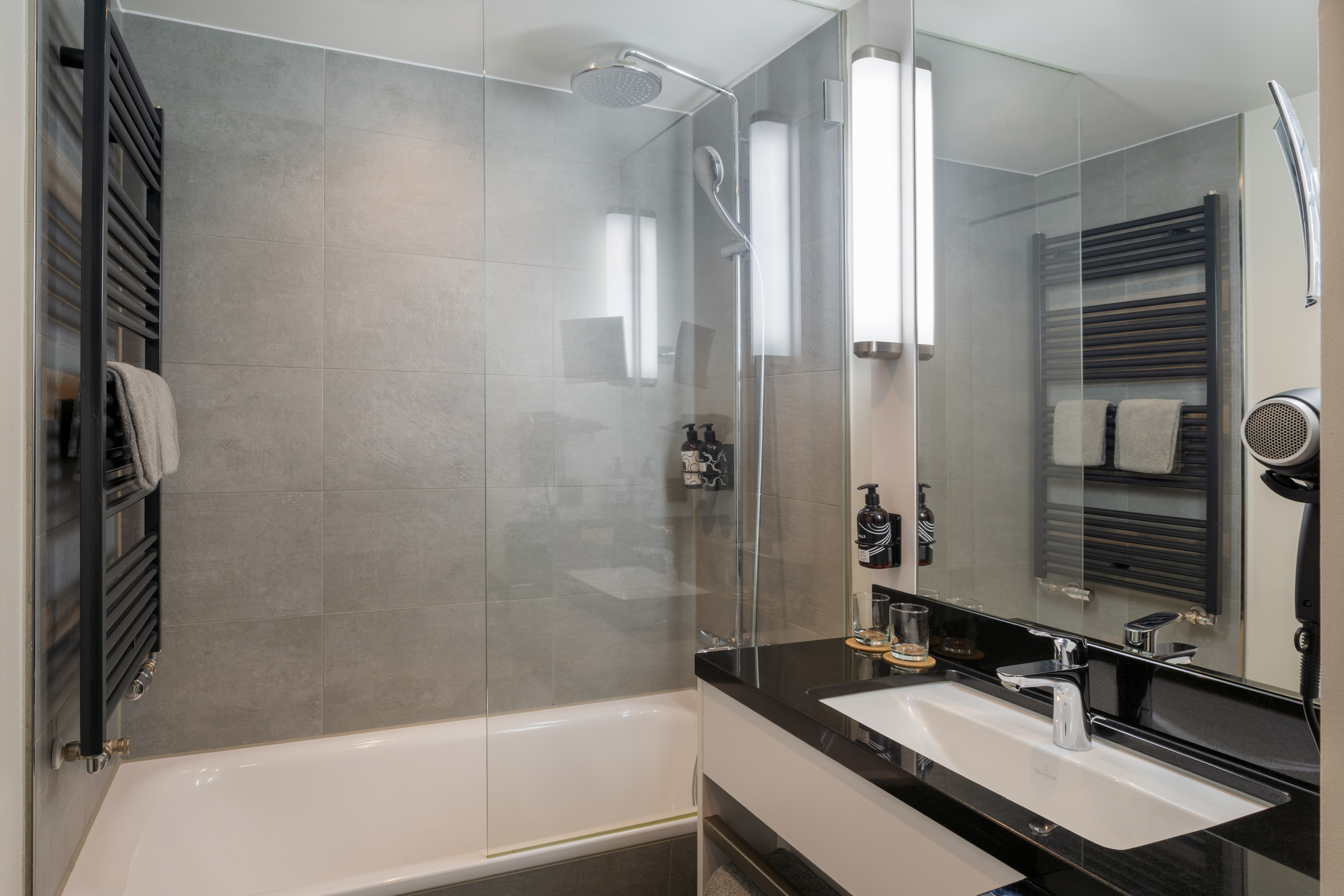 Modern hotel bathroom with shower-bathtub, vanity, grey tiles, towel warmer.
