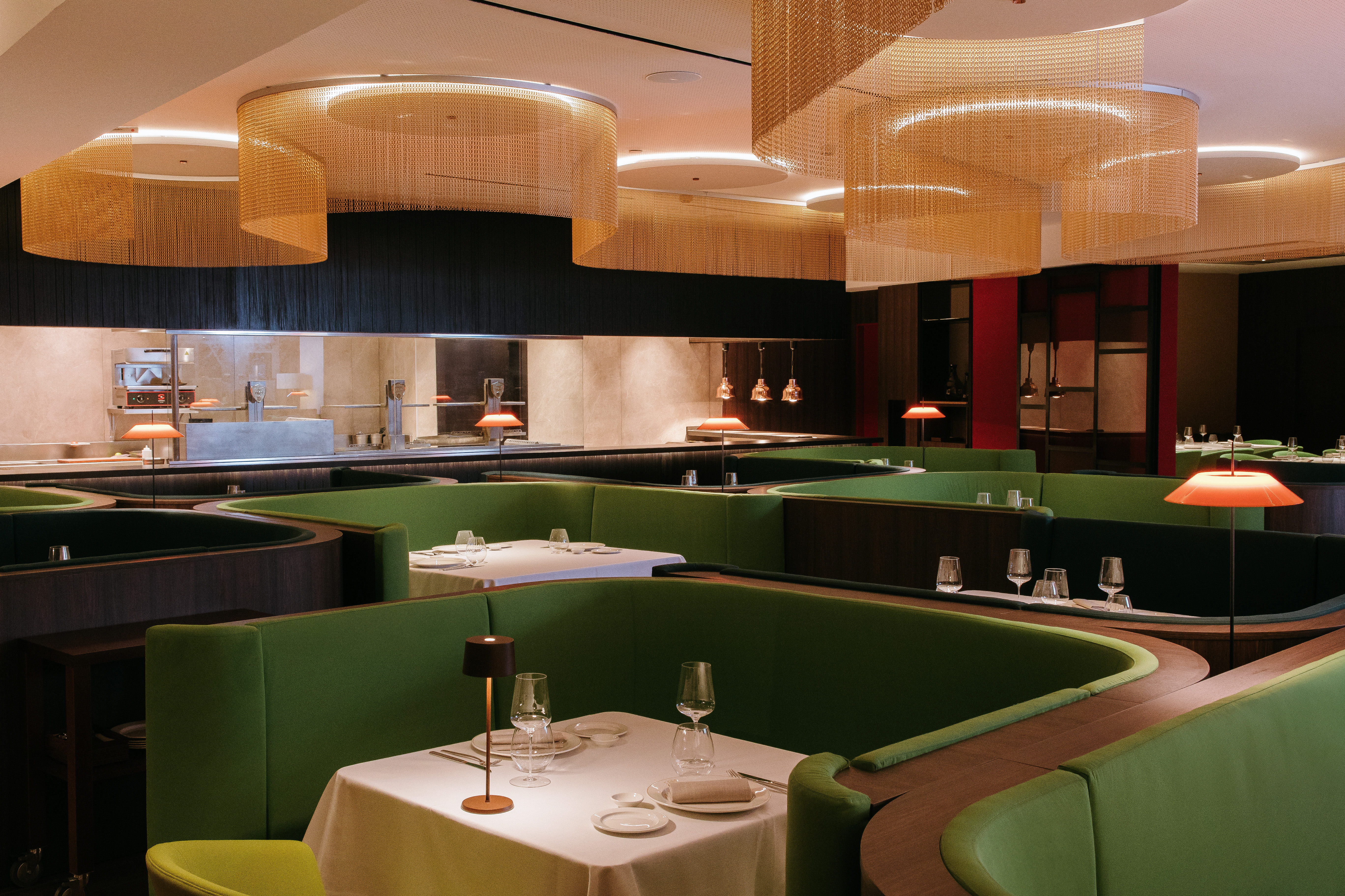 Modern restaurant with green curved booths, gold ceiling decor, and open kitchen.