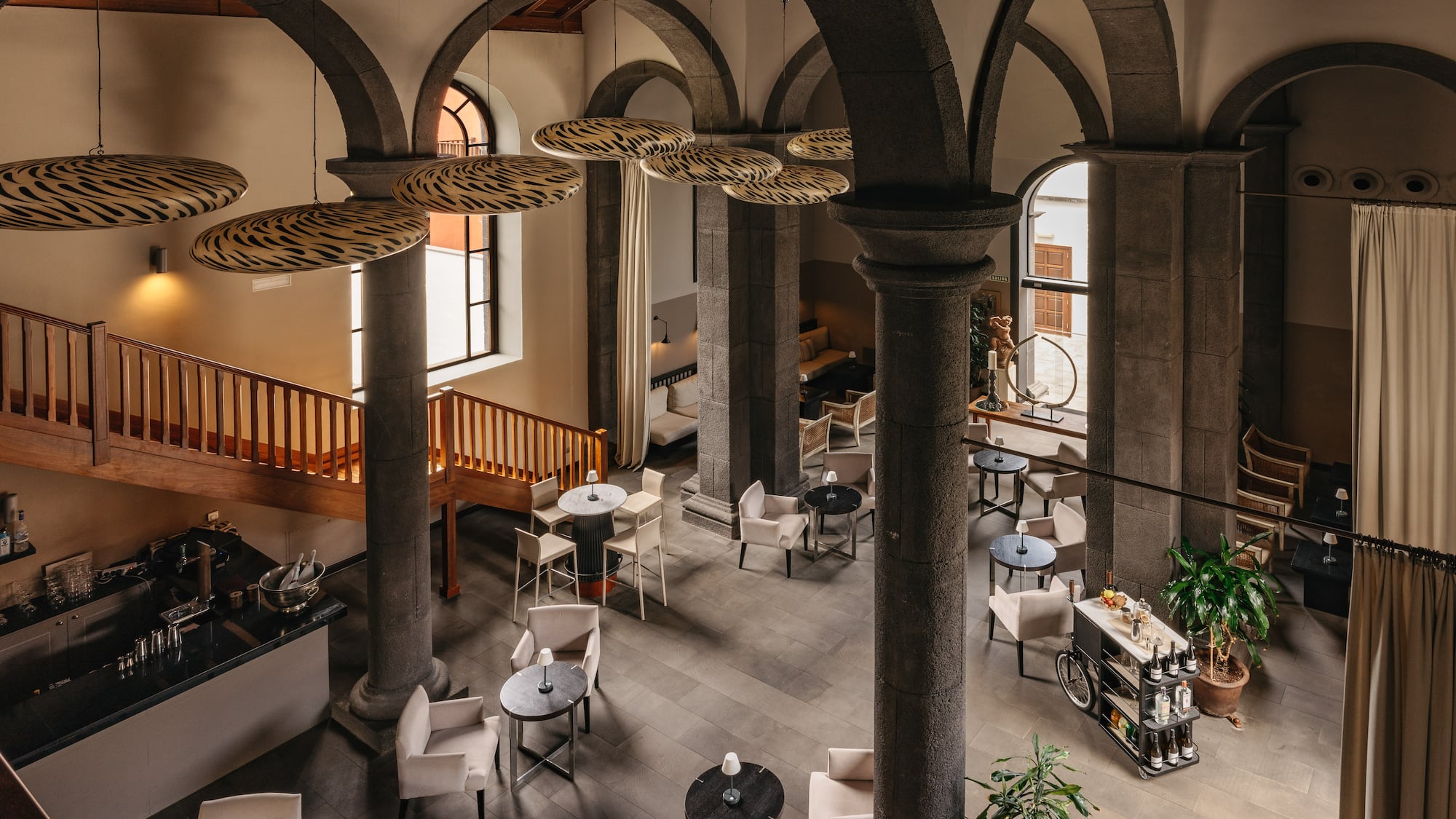 Modern hotel lounge with stone arches, zebra lights, bar, and elegant seating.