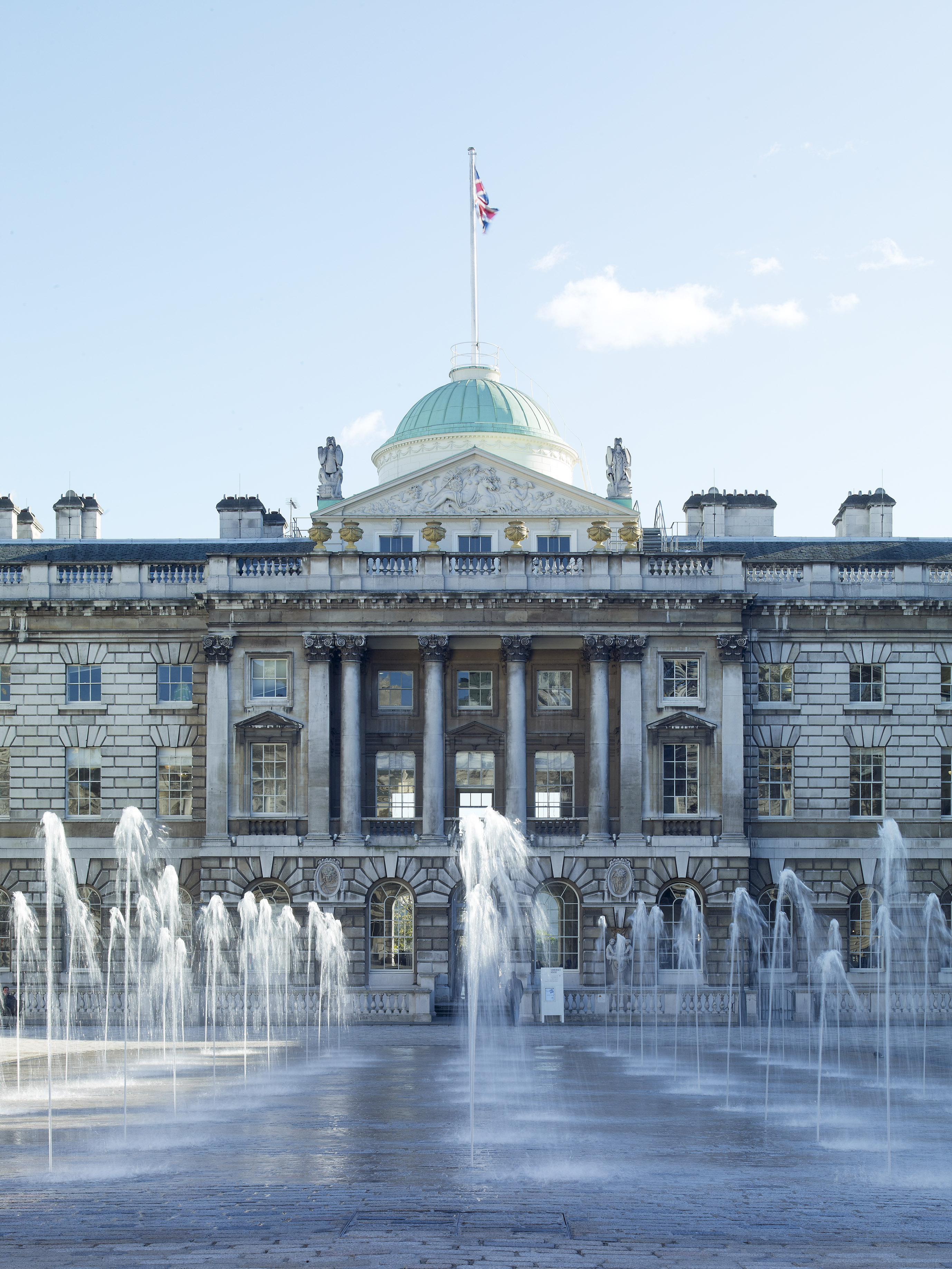 Somerset House, Londres, con fuentes de agua en primer plano y bandera británica.