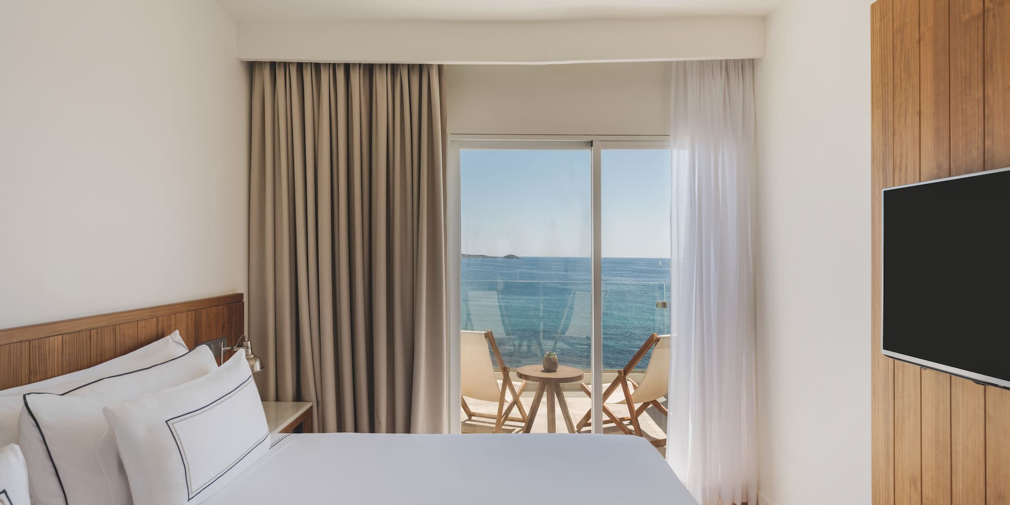Modern hotel bedroom with sea view balcony and wooden accents.