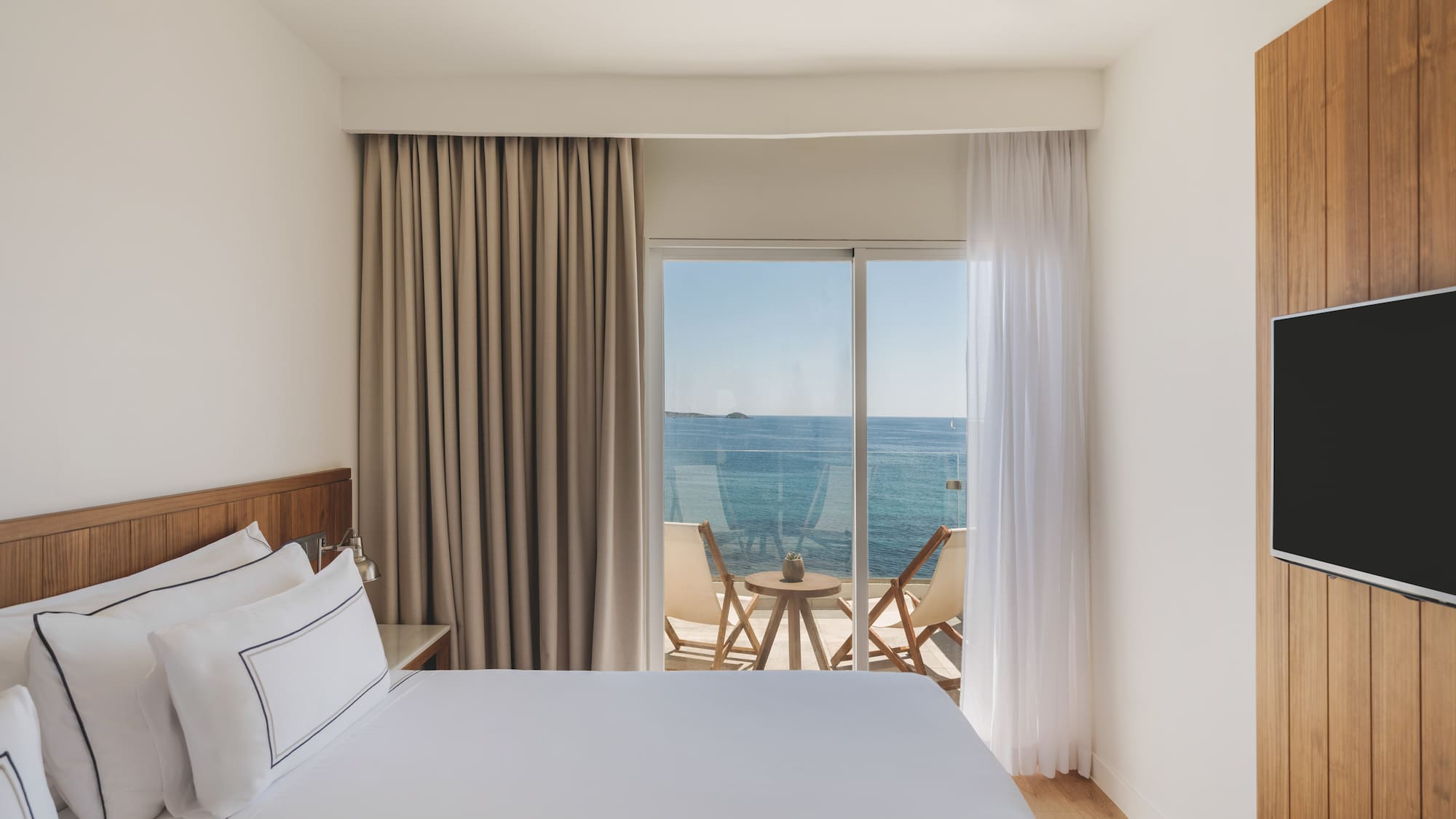 Modern hotel bedroom with sea view balcony and wooden accents.